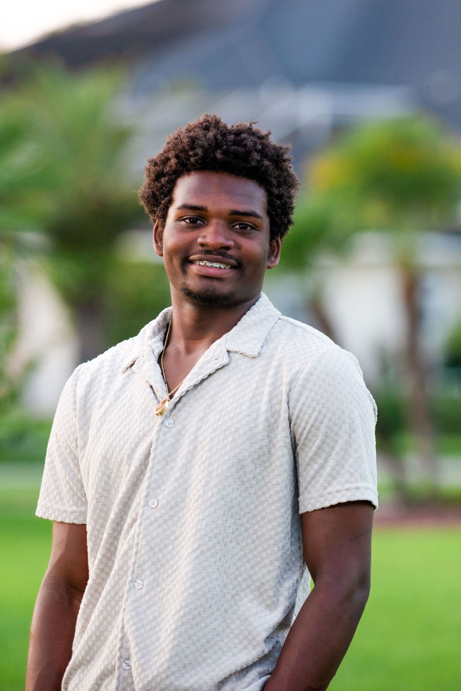 Person in white polo shirt smiling outdoors with greenery in background.