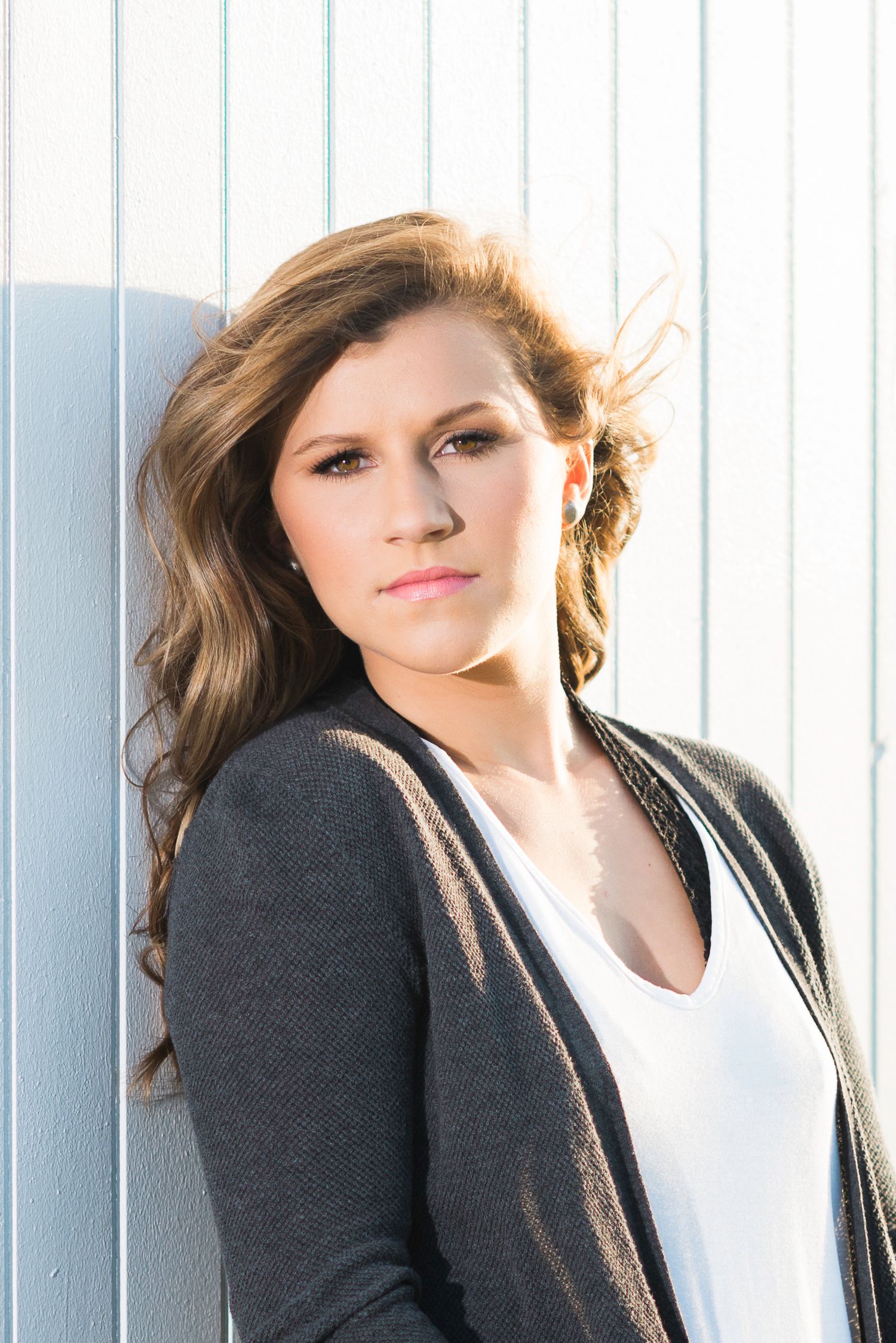 Fashion portrait against white vertical blinds with dramatic lighting.