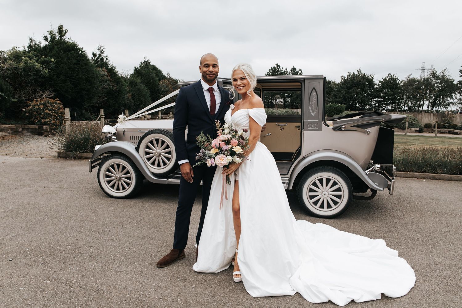 A wedding couple poses with their classic vintage car on their special day.