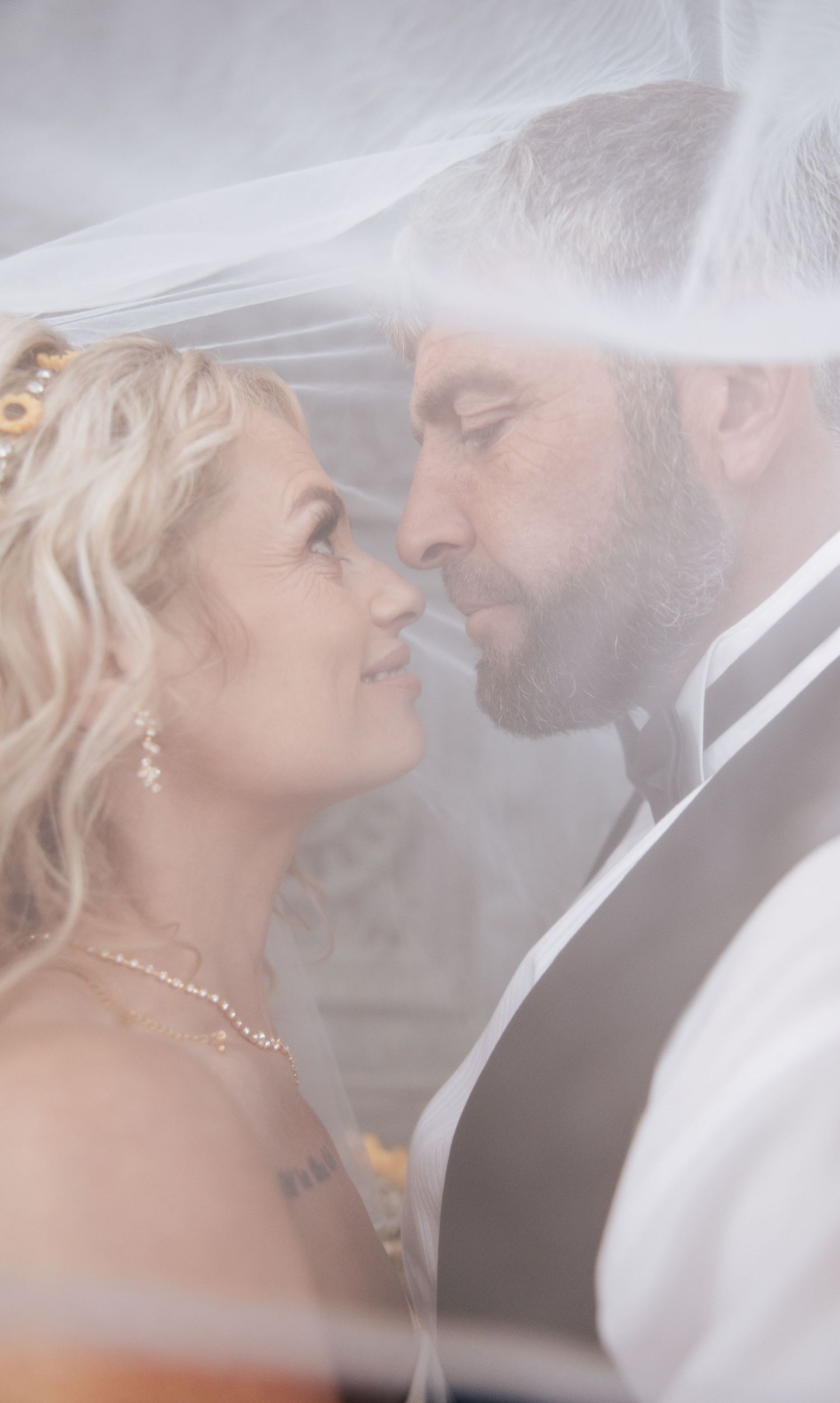 Bride and groom share an intimate moment under a wedding veil, gazing into each other's eyes on their wedding day.