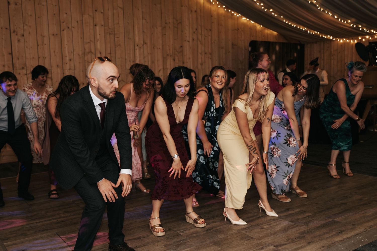 Guests dancing together at a rustic barn wedding reception with string lights overhead.
