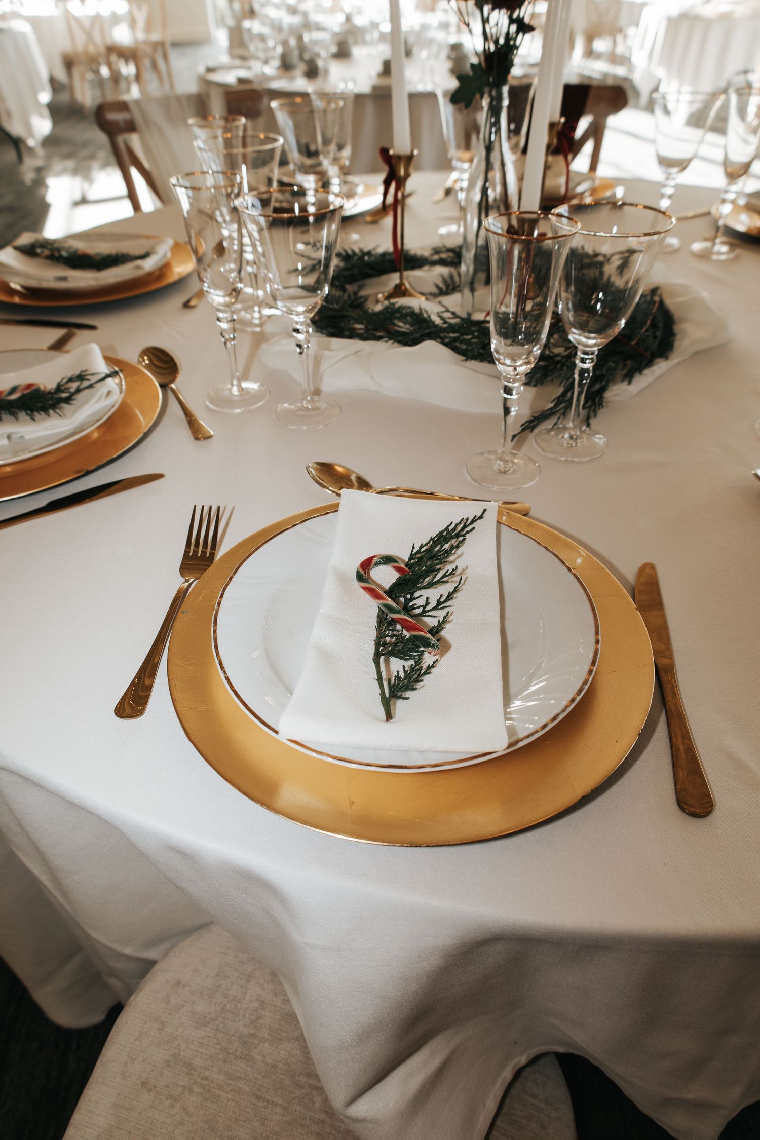 Elegant table setting with gold charger plate, white napkin, and evergreen sprig at a wedding reception.
