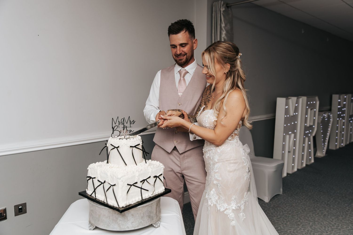 Bride and groom cutting their white three-tier wedding cake together at their wedding reception.