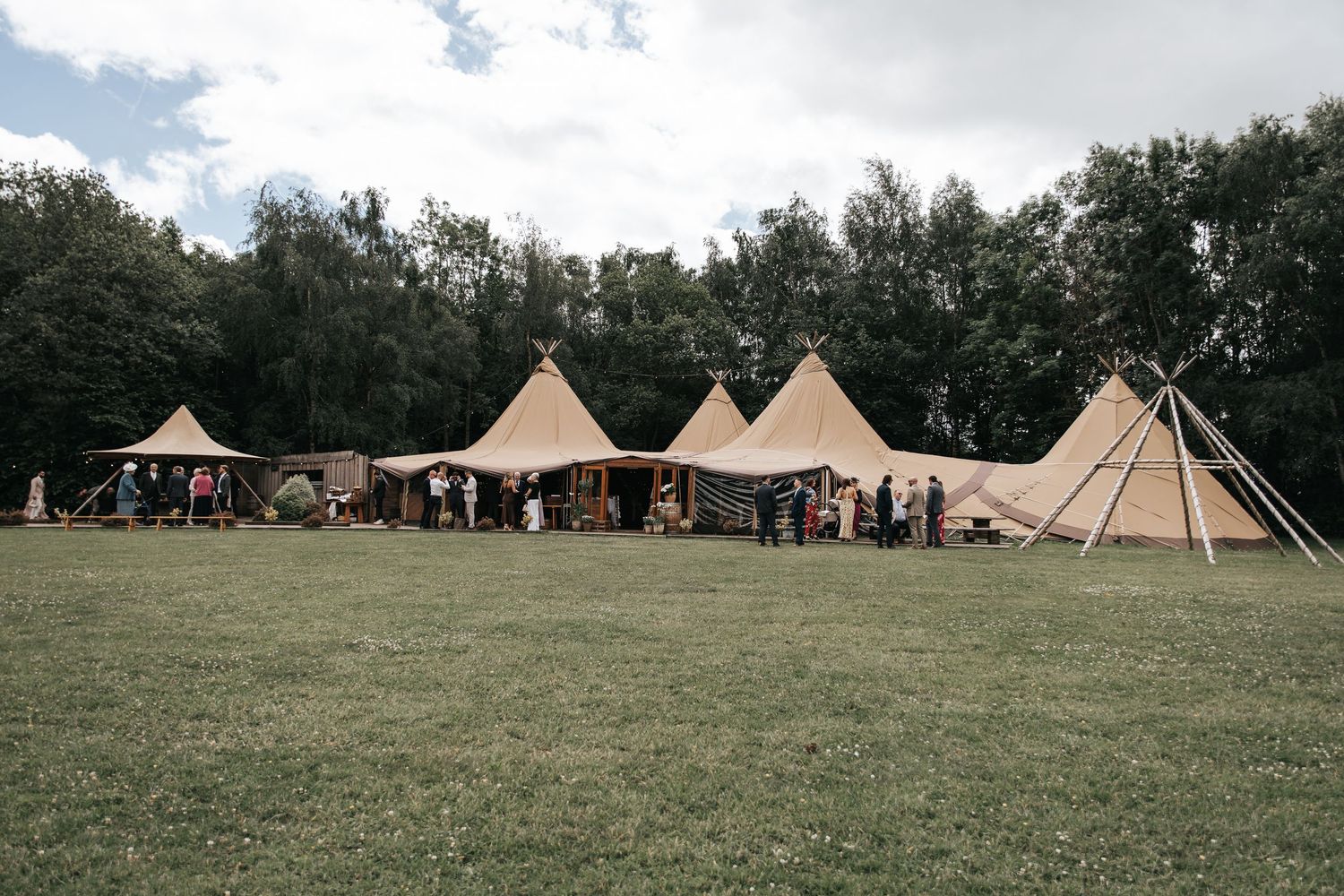 Rustic tipi tents set up on green meadow surrounded by trees for an outdoor festival or wedding event.