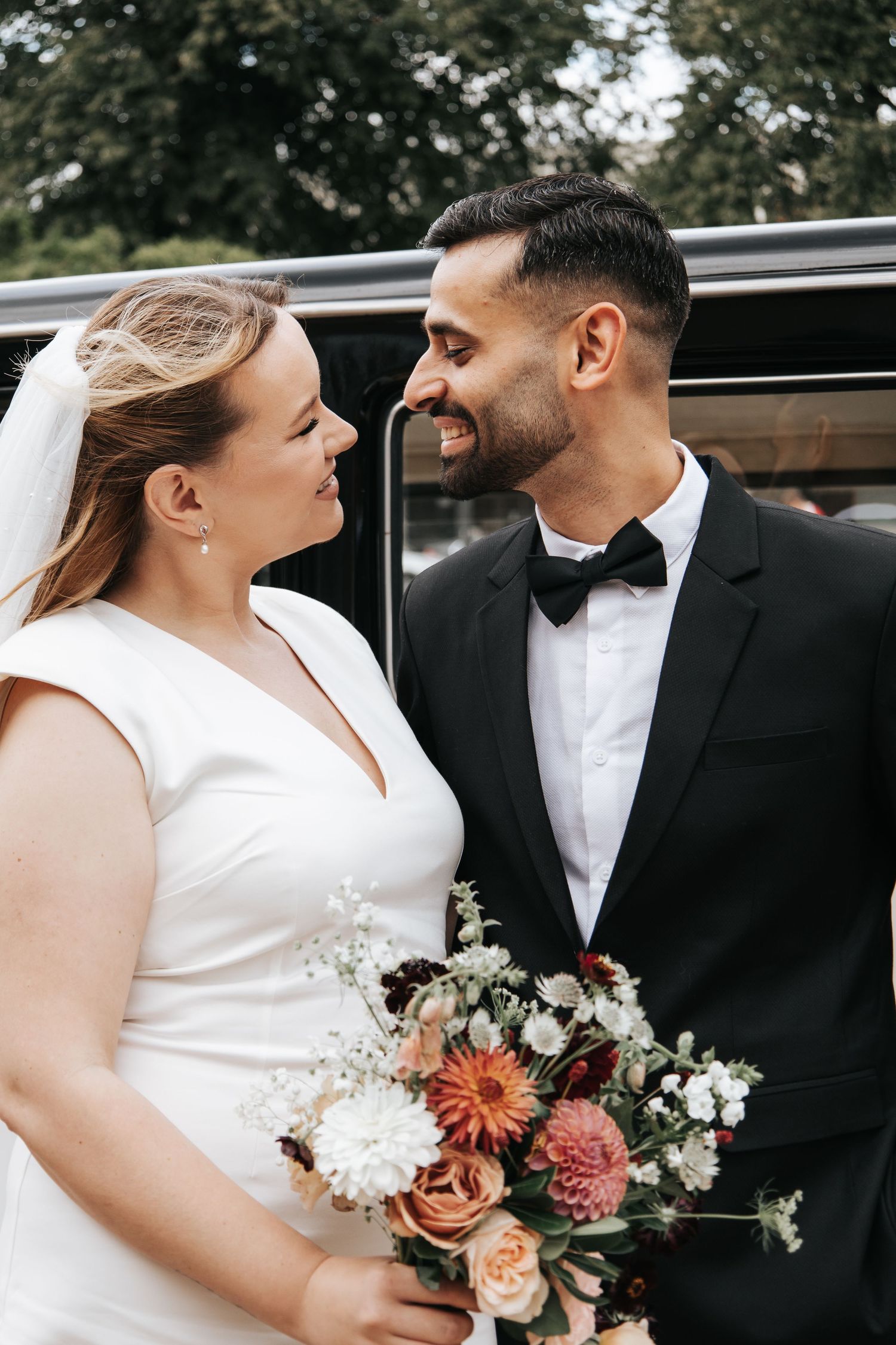 Bride and groom sharing intimate moment while holding floral bouquet.