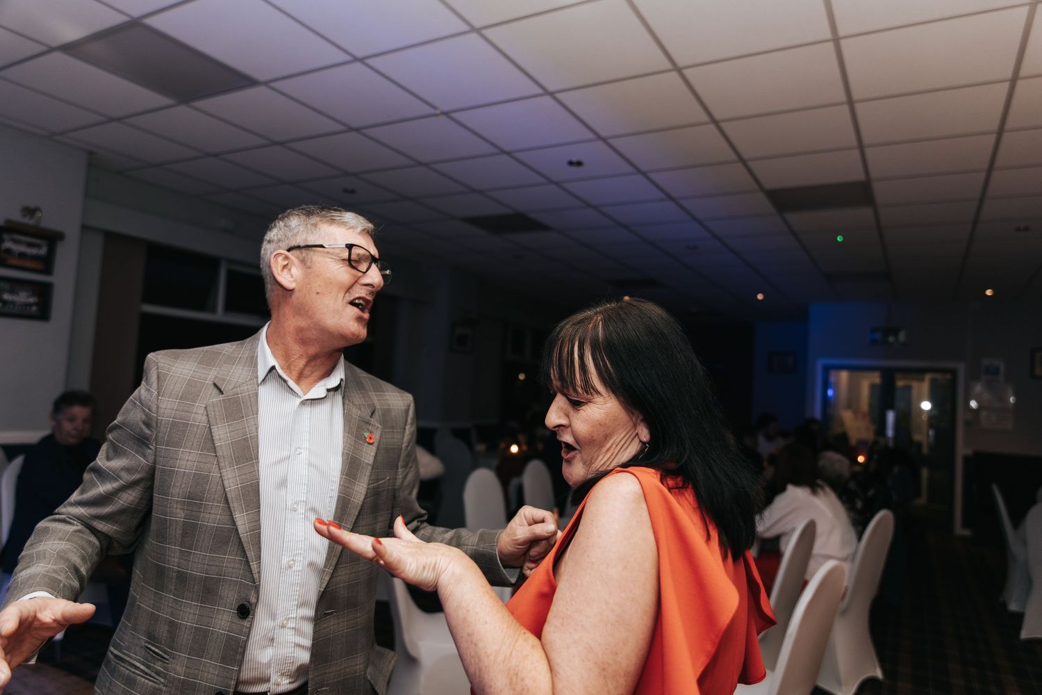 A group of people dancing and socializing at an indoor event with dim lighting and a festive atmosphere.