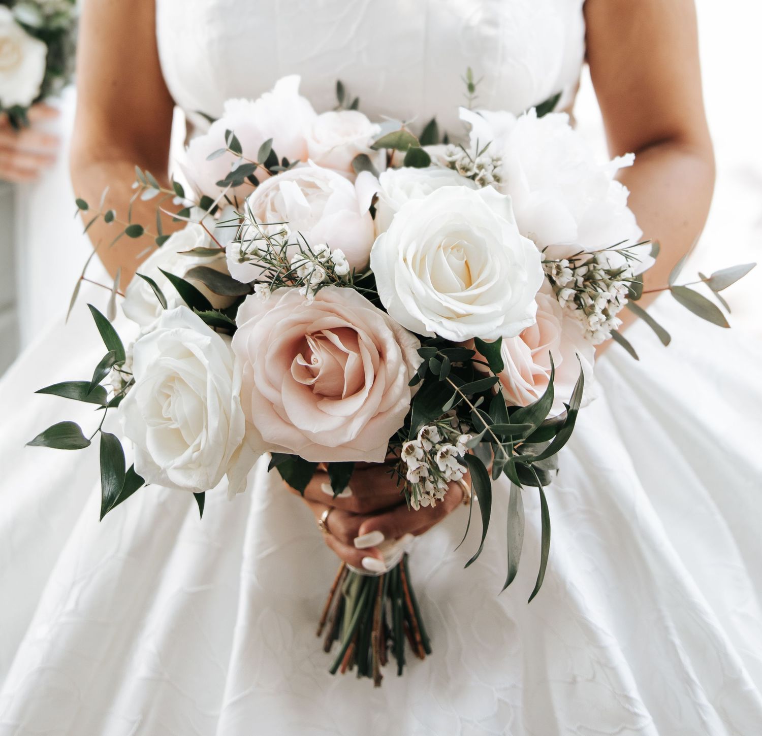 Bride holding a romantic wedding bouquet of blush pink and white roses with greenery accents.