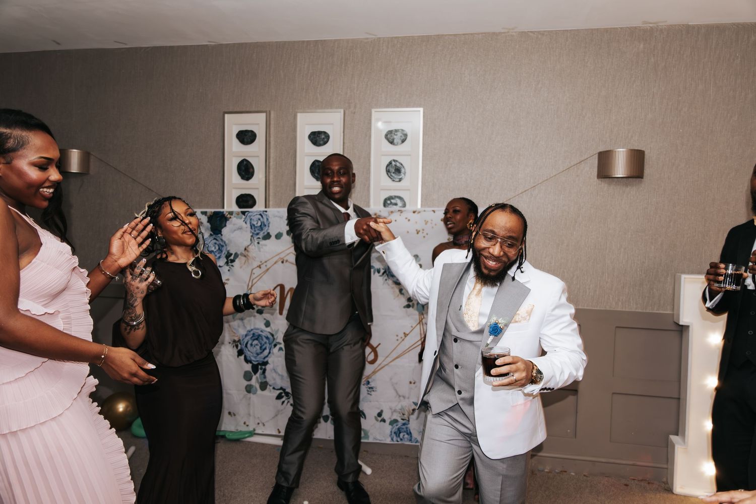 People dancing and celebrating at a party with guests wearing formal attire in a light colored indoor space.
