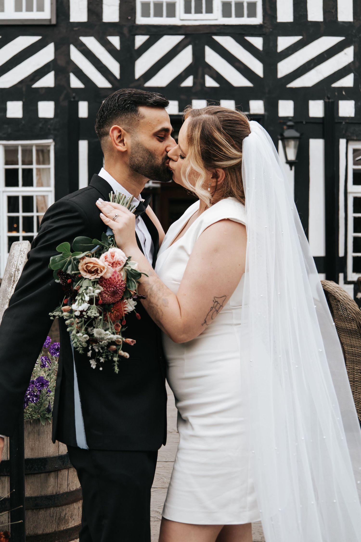 Wedding couple shares intimate moments against Tudor-style building with black and white timber framing.