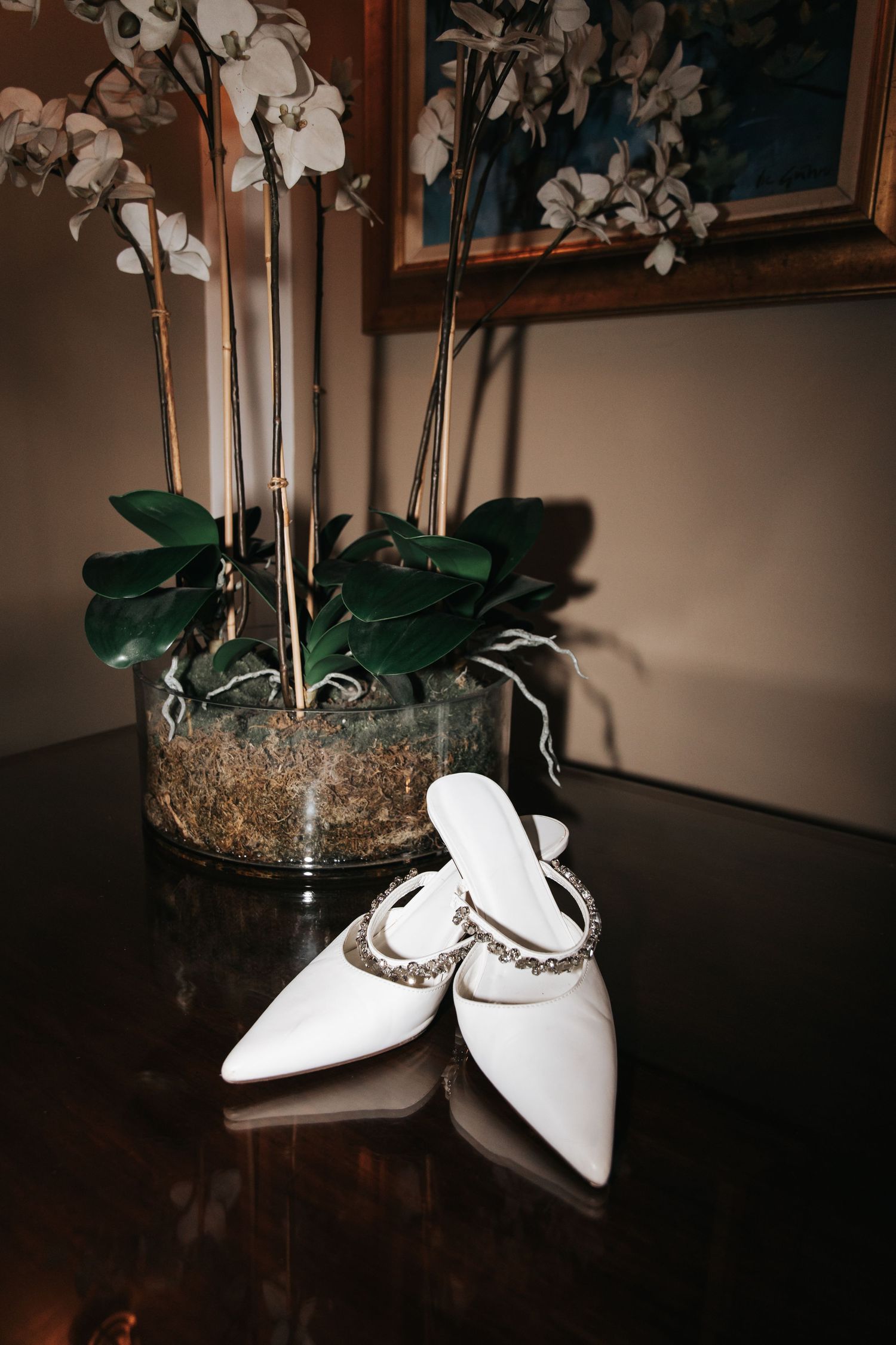 White bridal shoes displayed with delicate orchid flowers and decorative elements in an elegant indoor setting.