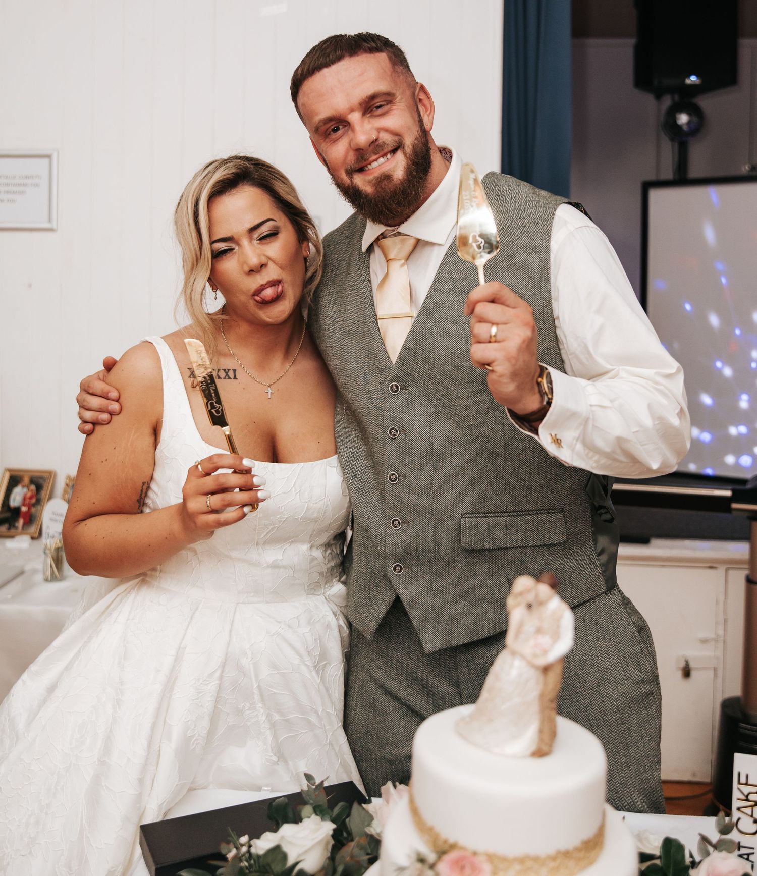 Bride and groom smiling together holding sparklers beside their wedding cake at their reception.
