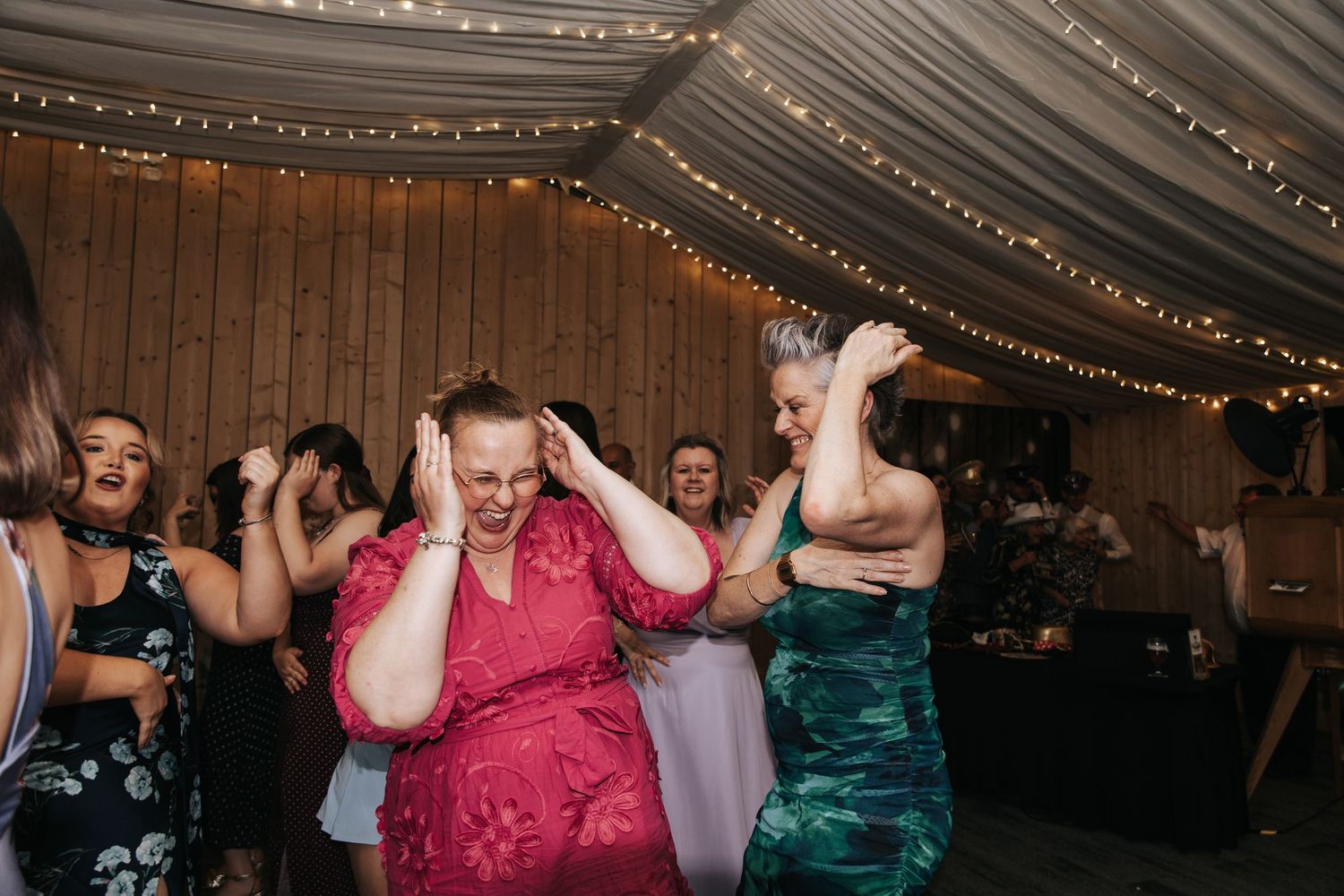 Guests in formal attire dancing and celebrating joyfully at a wedding reception with fairy lights.