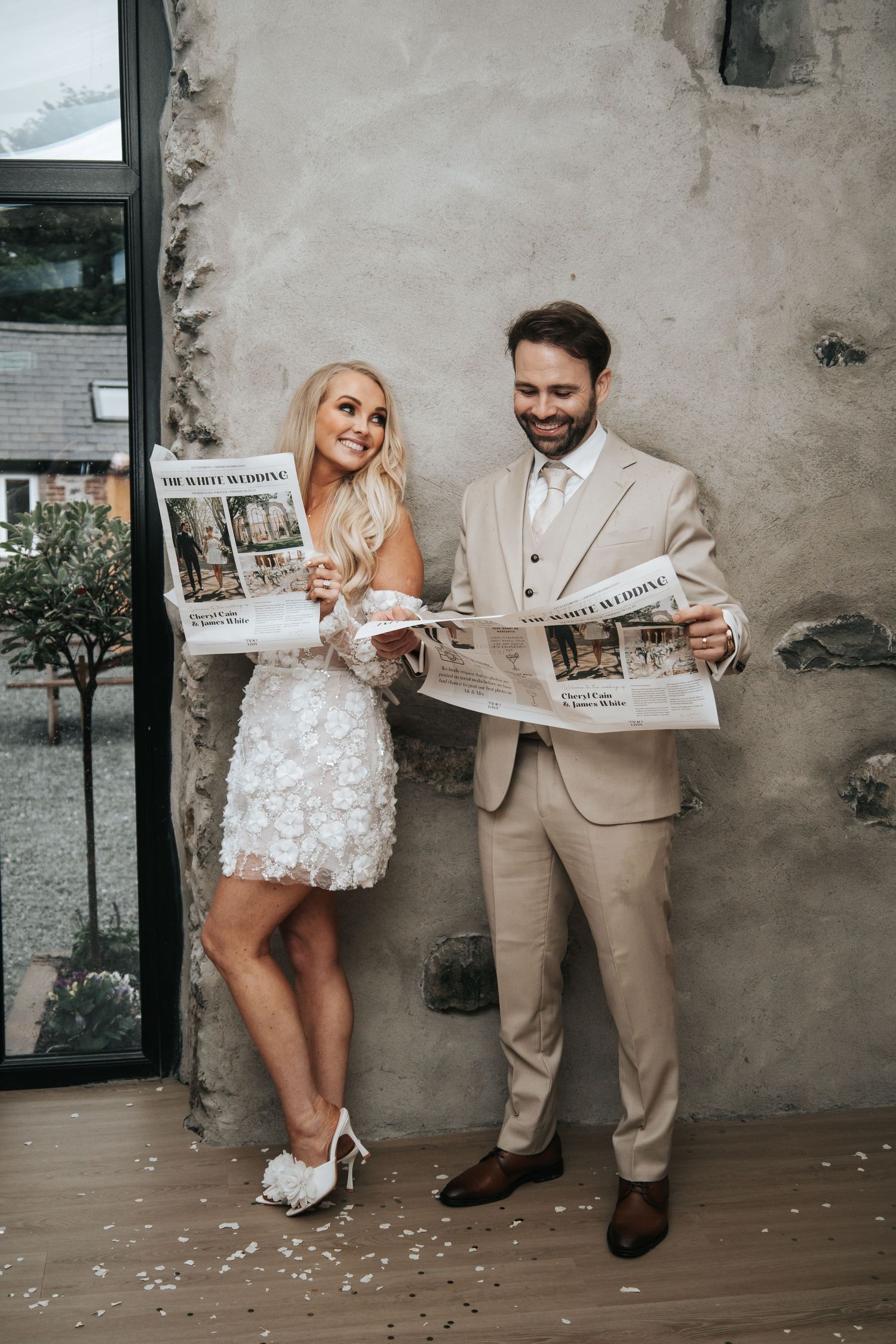 Playful couple reads newspapers together during wedding photo session.
