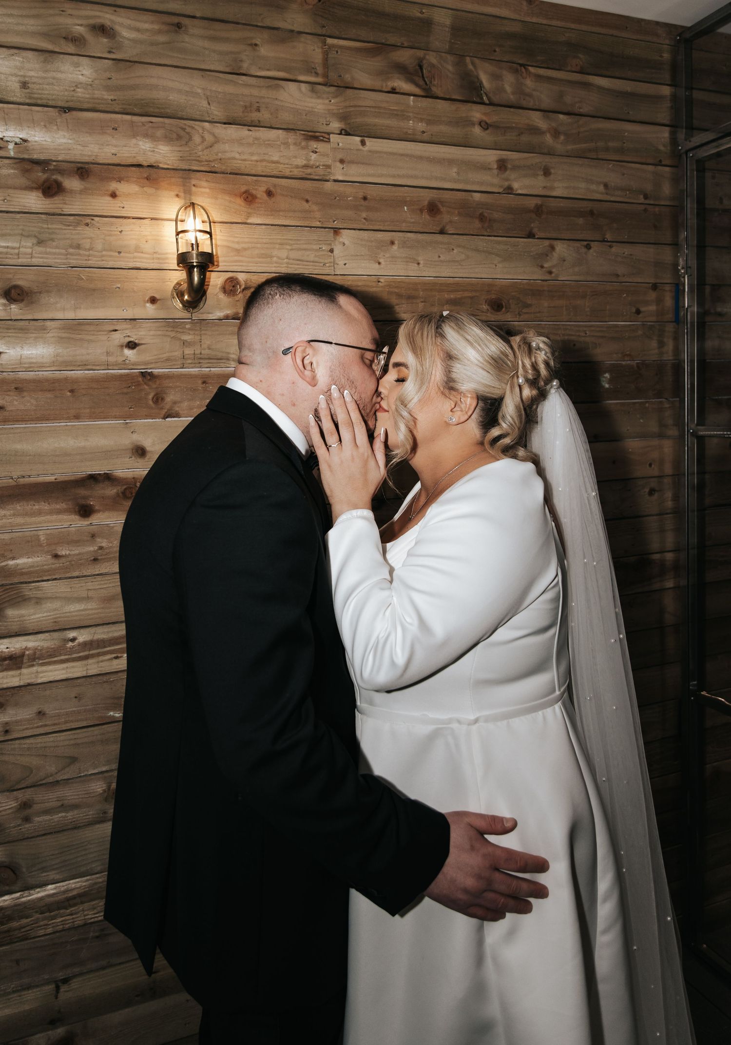 Romantic moment against rustic wooden wall backdrop at wedding venue.