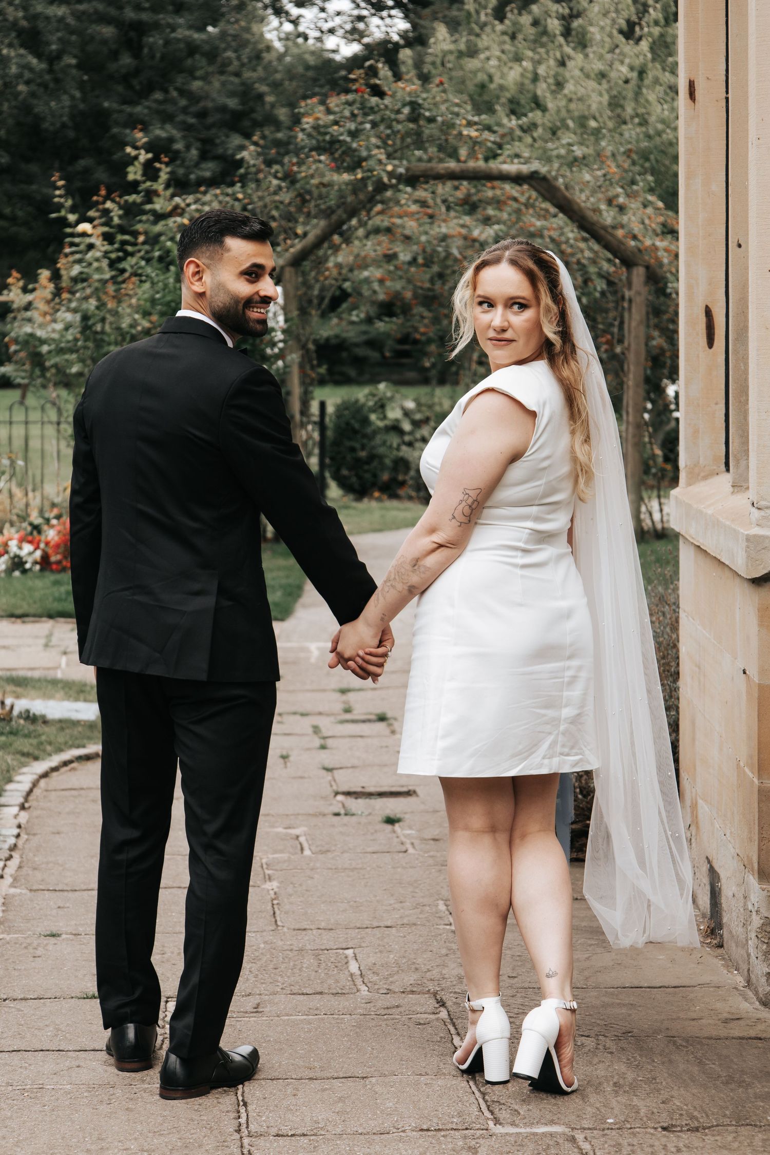 A wedding couple walks along a stone pathway under a covered outdoor walkway.