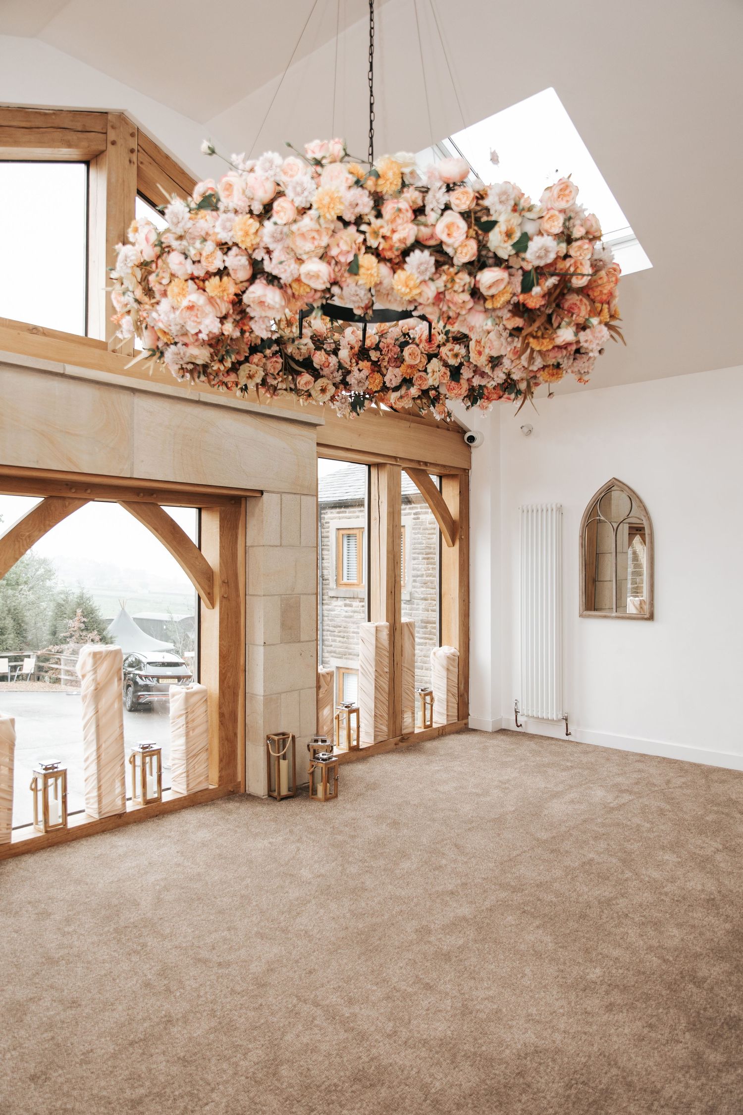 Elegant wedding venue with floral chandelier, oak beams, skylight, and beige carpet in a bright, airy room.