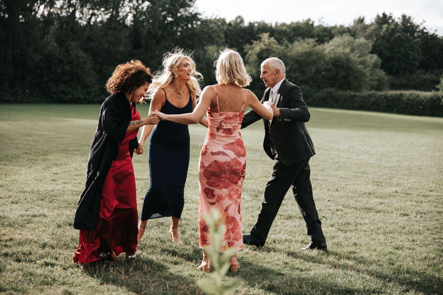 Four elegantly dressed adults dancing together on a green lawn at an outdoor wedding reception.