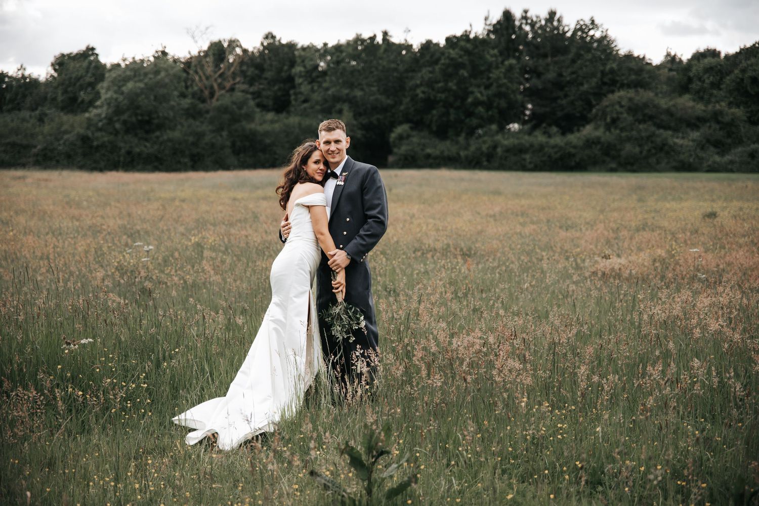 Bride and groom embracing in a lush meadow field, wearing wedding dress and suit on their special day.