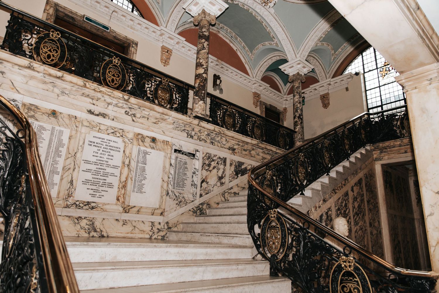 Ornate marble staircase with wrought iron railings and decorative arched ceiling in a grand historic building.