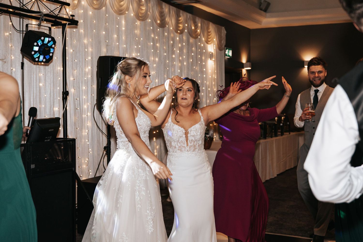 Wedding guests dance and celebrate together on a dimly lit dance floor during an evening reception.