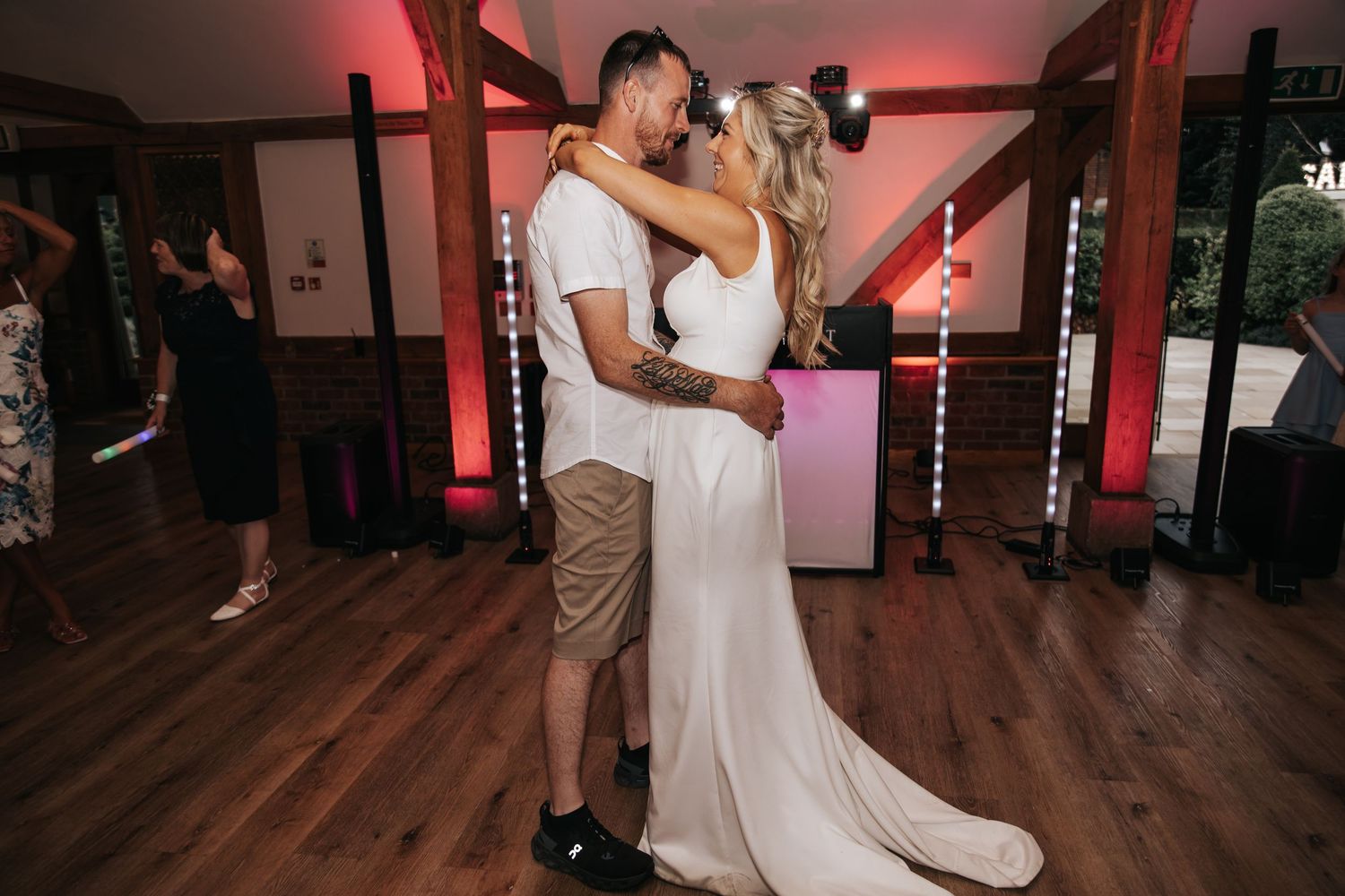 Bride and groom share romantic first dance in elegant wedding venue with warm red ambient lighting.