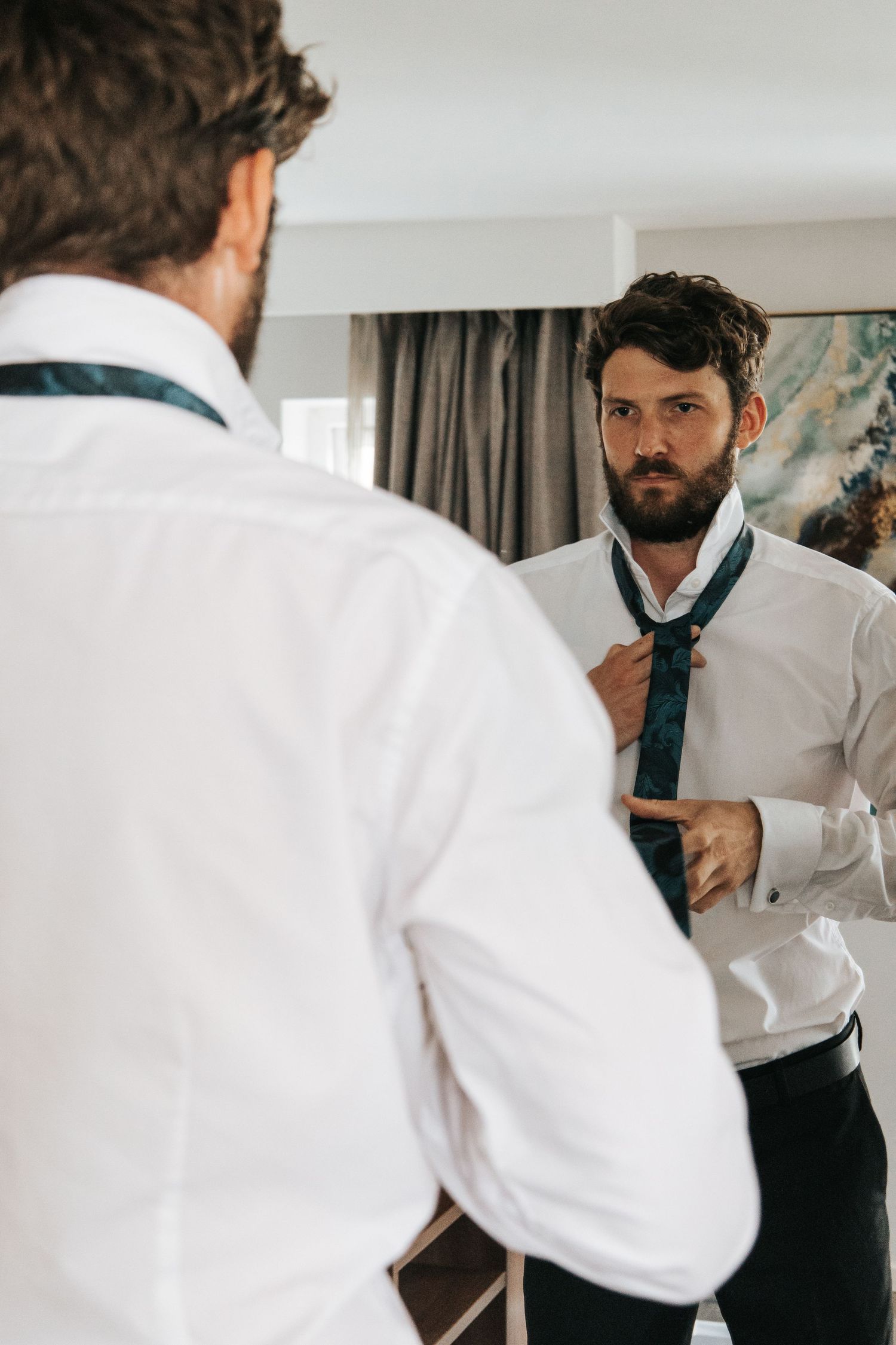 Close-up of a man adjusting his tie while getting dressed in formal attire.