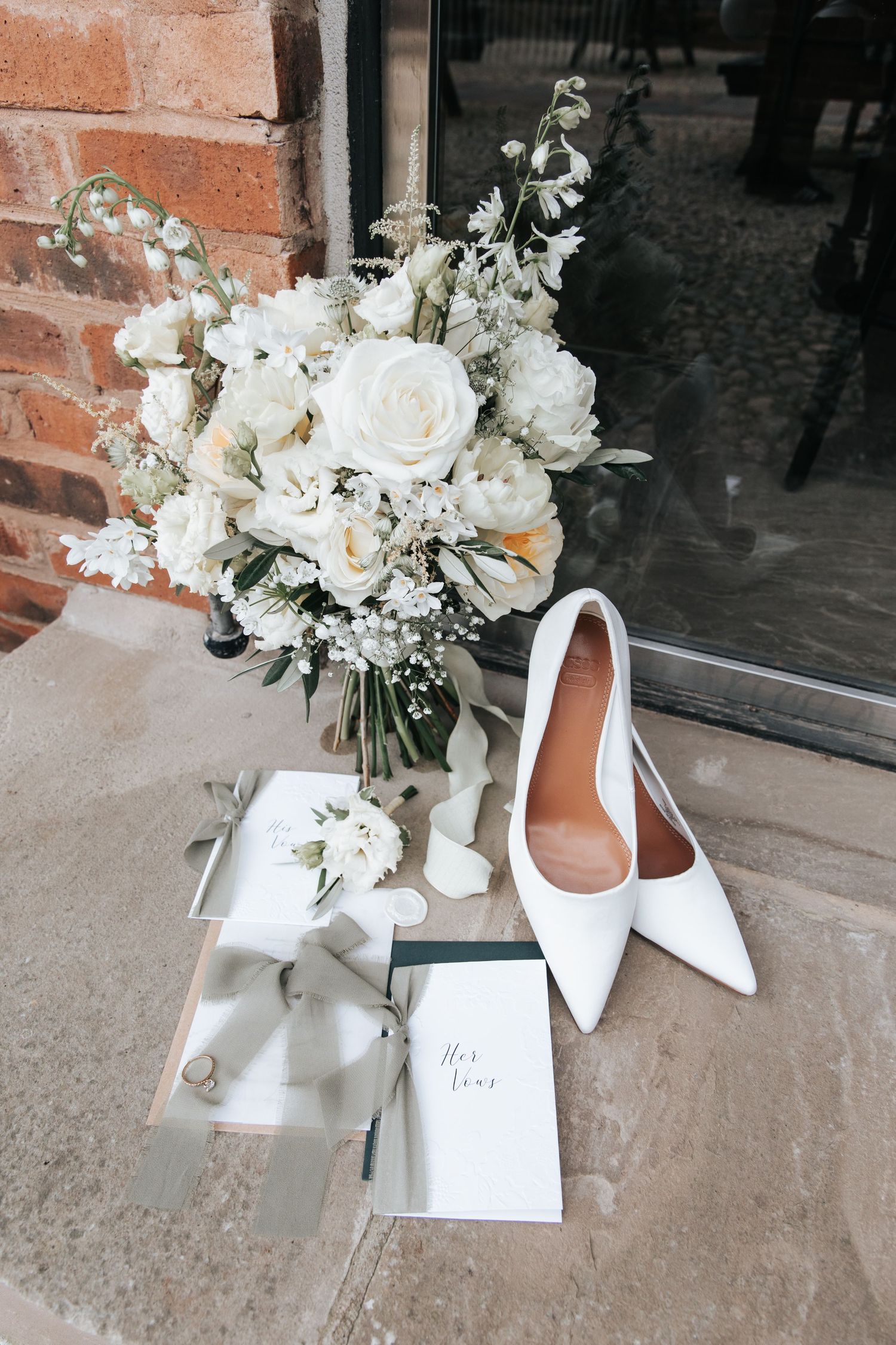 Elegant white bridal shoes and floral bouquet arranged with white flowers and greenery on a stone surface.