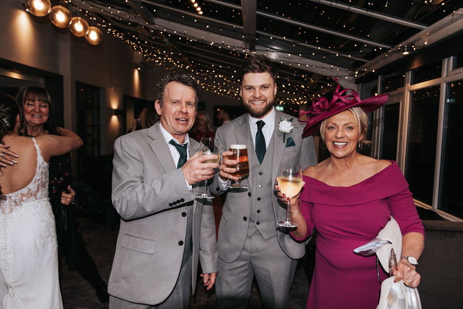 Wedding guests dancing and celebrating at an evening reception with string lights overhead.