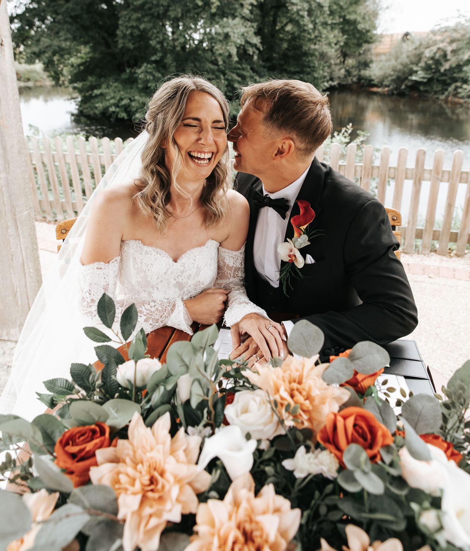 A joyful bride and groom share a romantic moment at their wedding table, surrounded by elegant floral arrangements.