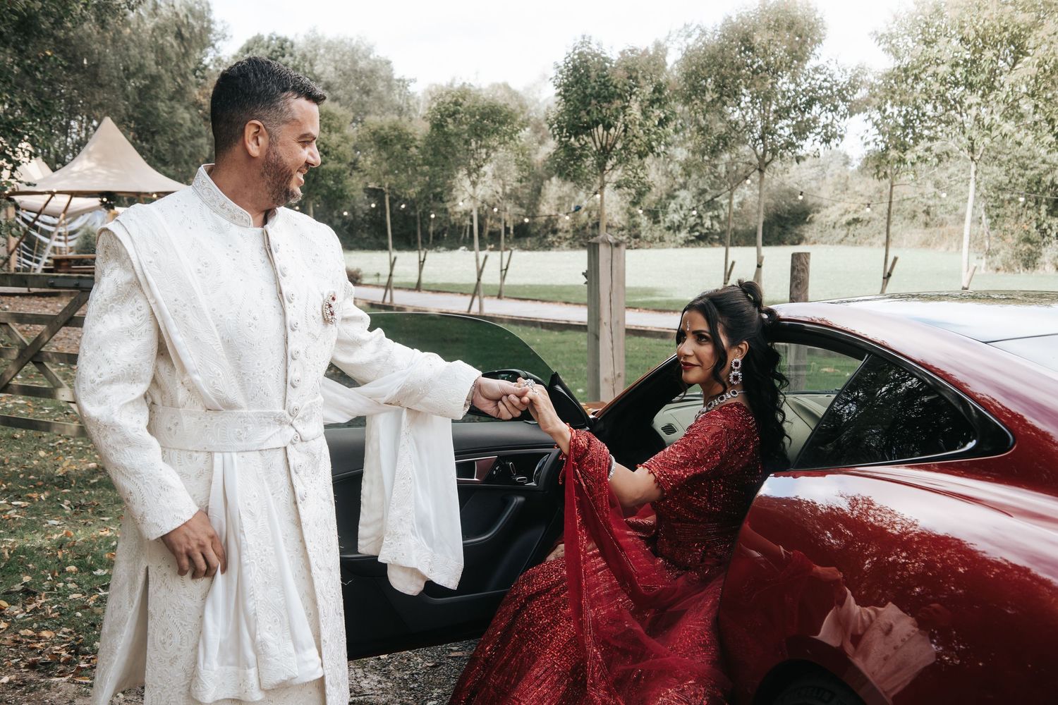 Wedding couple posing near luxury cars with bride in white and red accents.