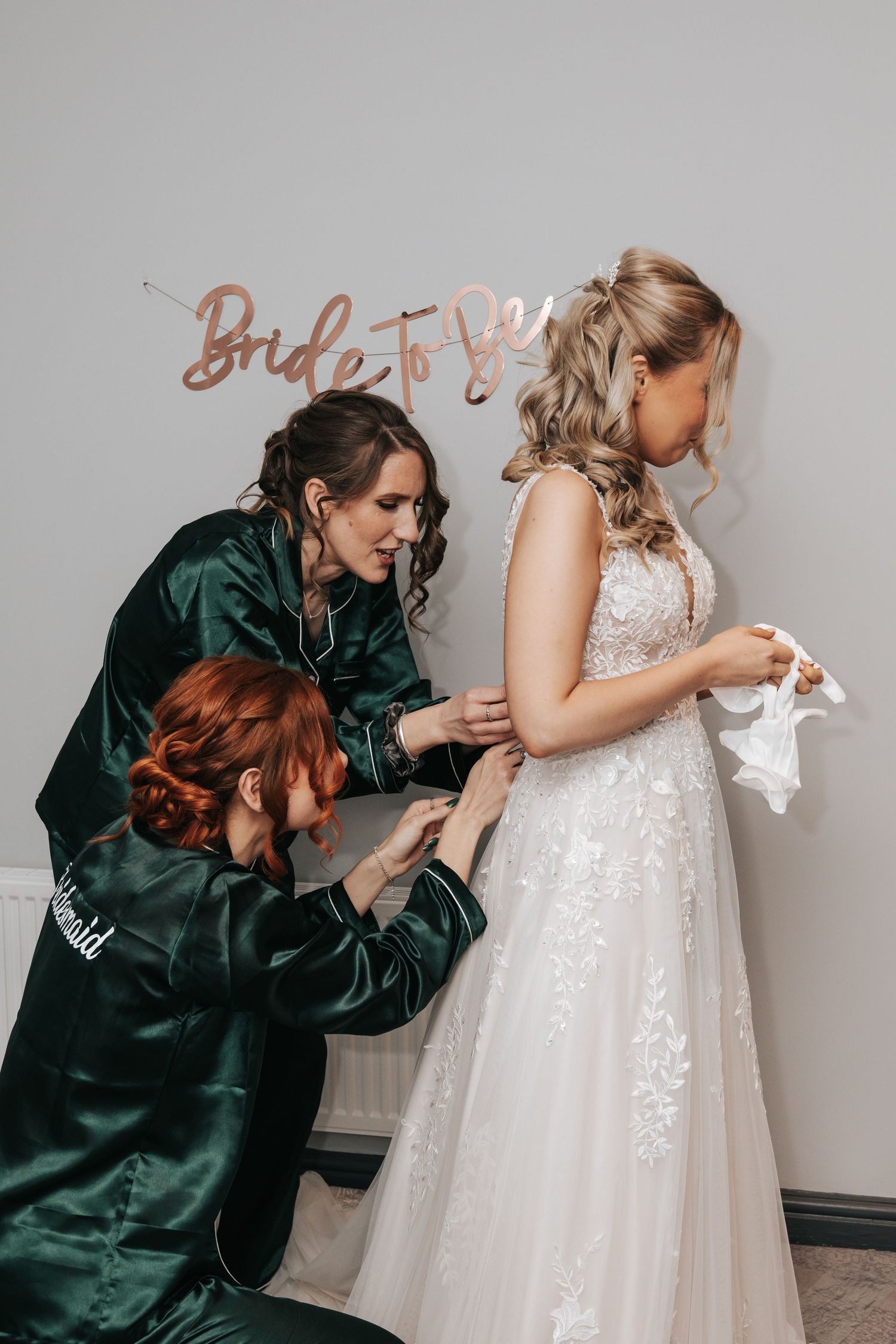 Wedding party members help with final dress preparations in getting ready room.