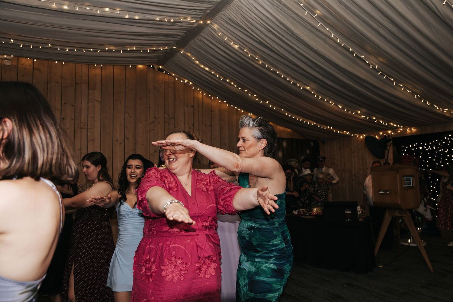 Two women dancing together energetically at a wedding reception decorated with string fairy lights.