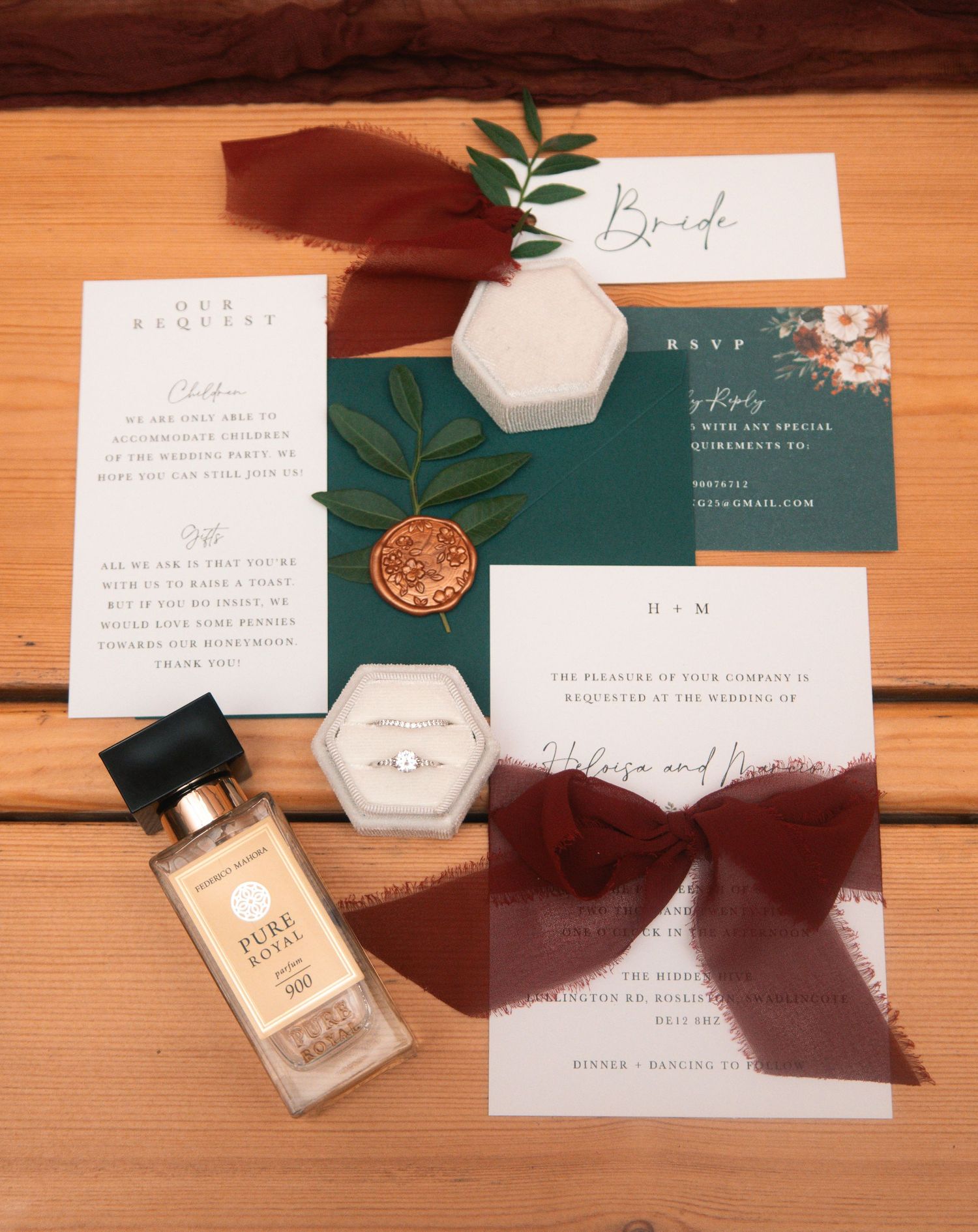 Wedding stationery set with green accents, perfume bottle and ring box on wooden surface.