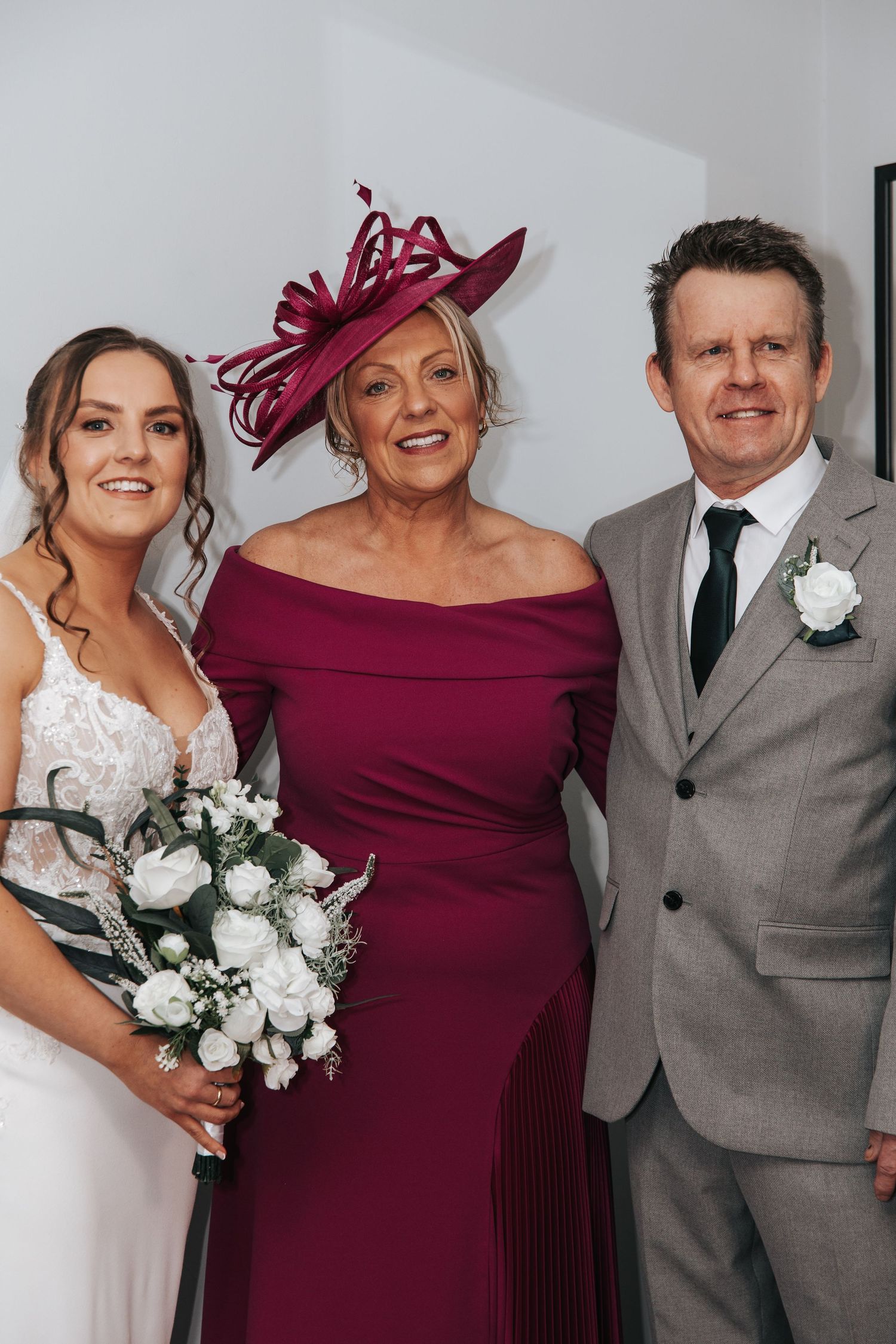 Wedding party members in burgundy dress and grey suit pose with bride in white.