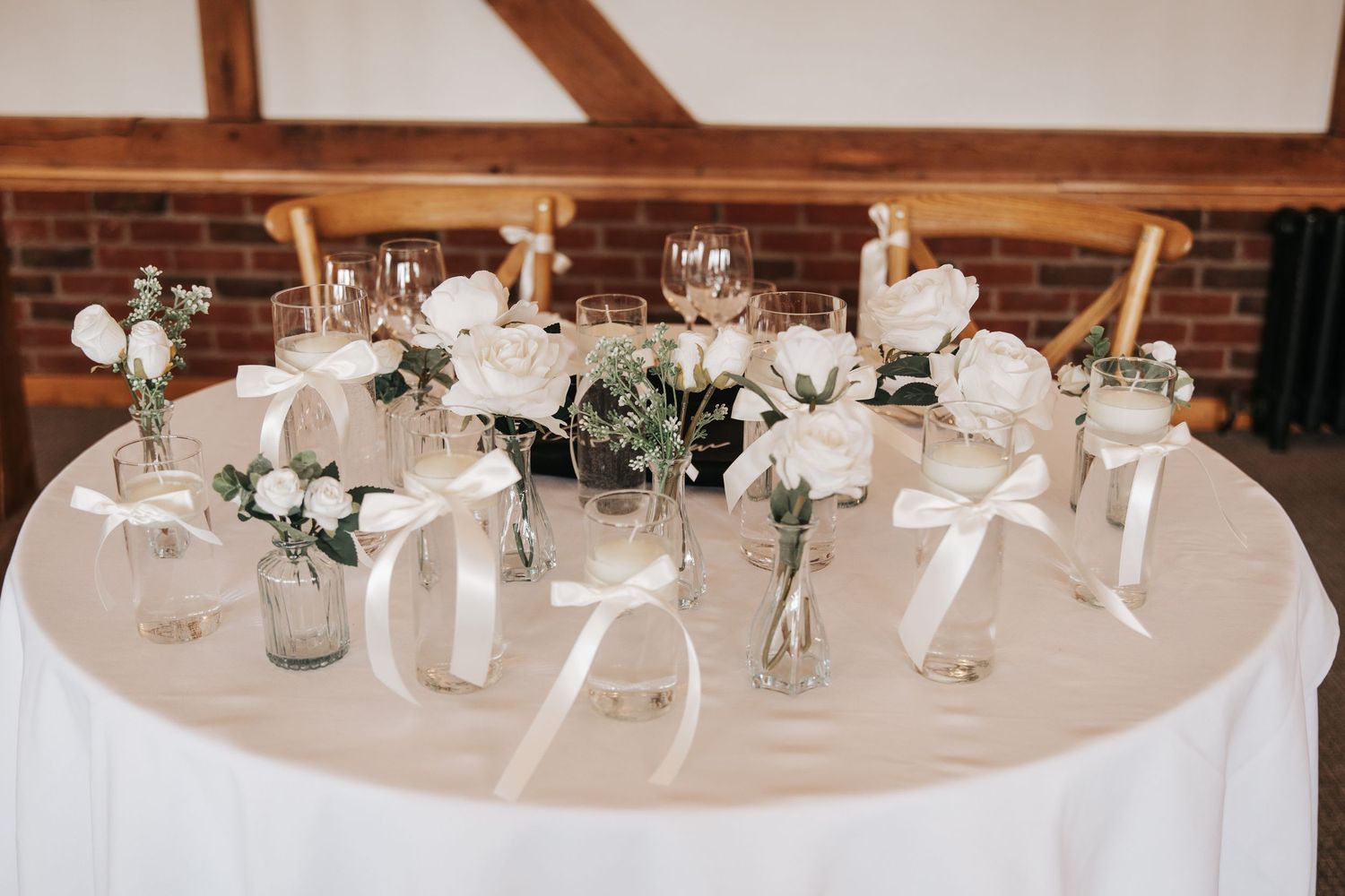 Elegant wedding sweetheart table with white rose centerpieces in glass vases tied with satin ribbons.