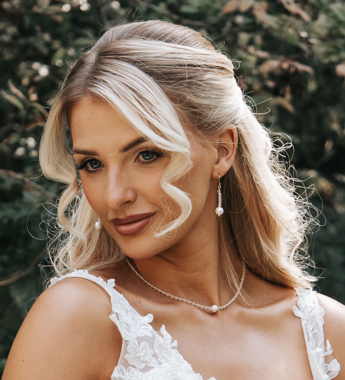 Artistic bridal portrait highlighting elegant jewelry and romantic hairstyle in natural setting.