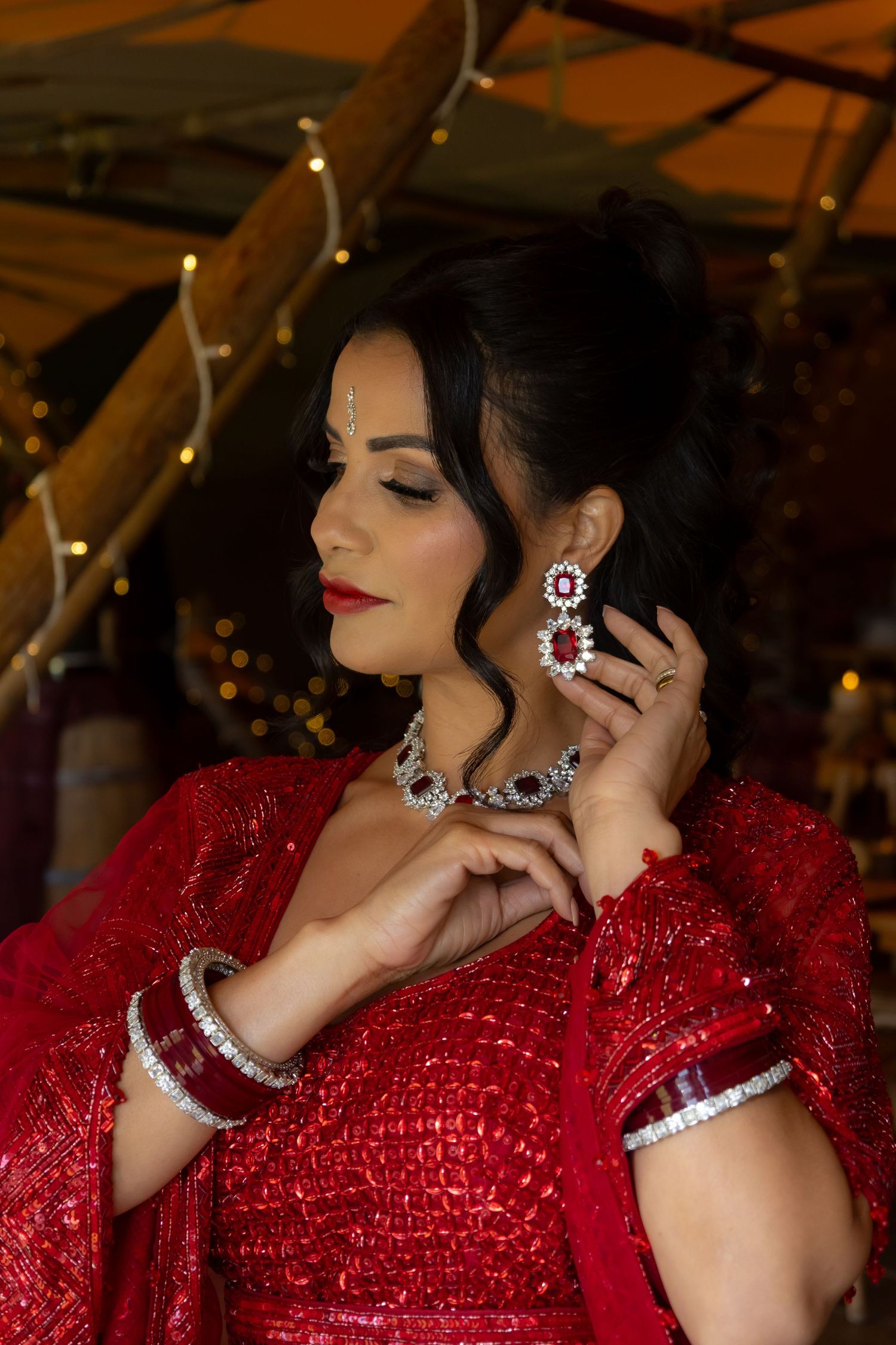 Elegant poses in a sequined red evening gown with diamond jewelry under warm lighting.