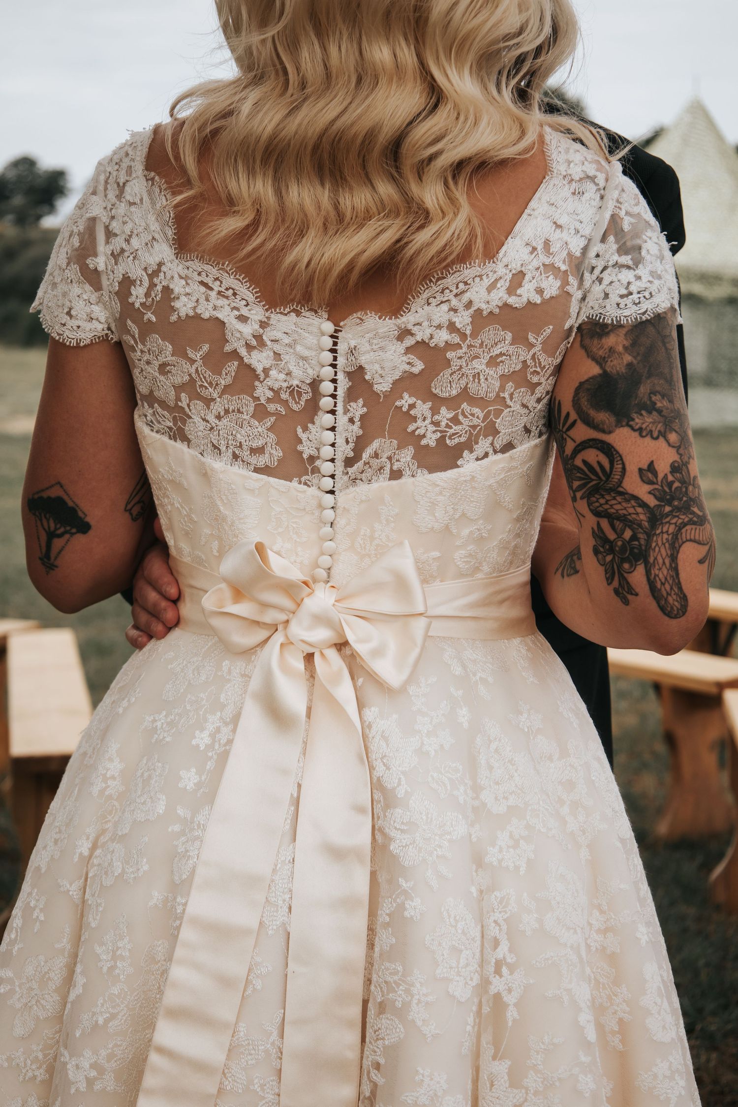 Back detail of lace wedding dress with delicate buttons and peach satin bow.