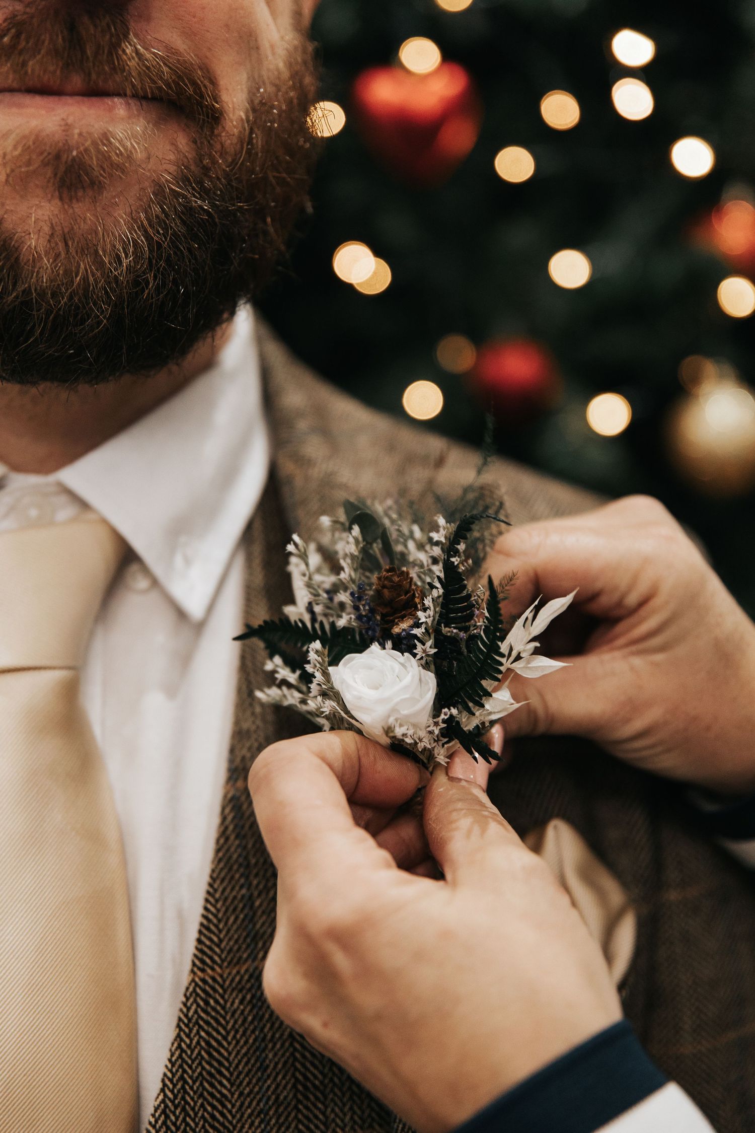 Close-up of hands pinning boutonniere on groom's lapel with bokeh lights in background.