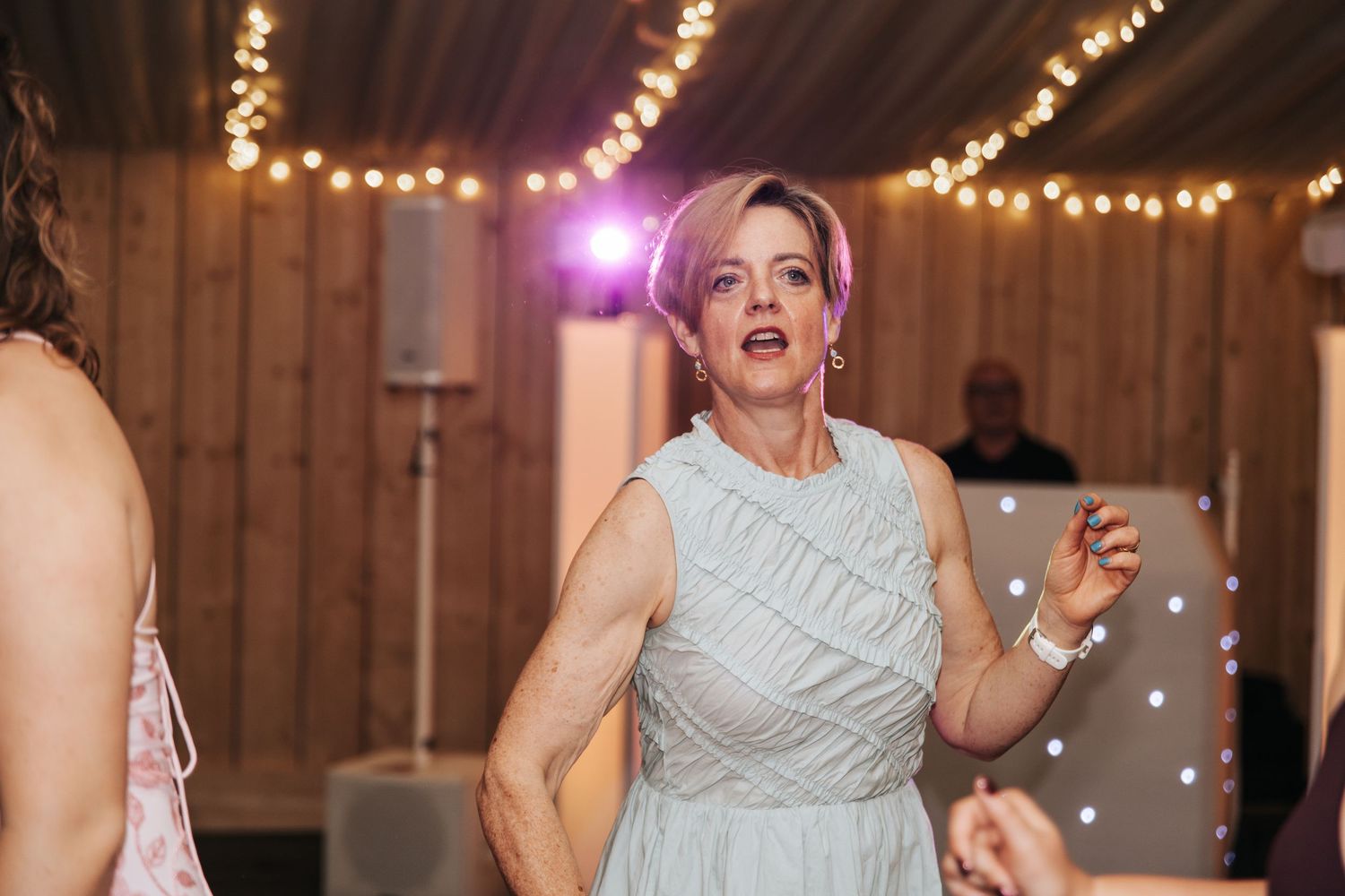 Woman in light blue dress dancing at a wedding reception with fairy lights in the background.