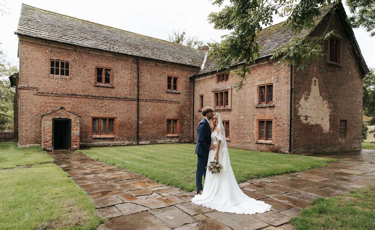 Bride and groom standing outside a historic red brick manor house on their wedding day.