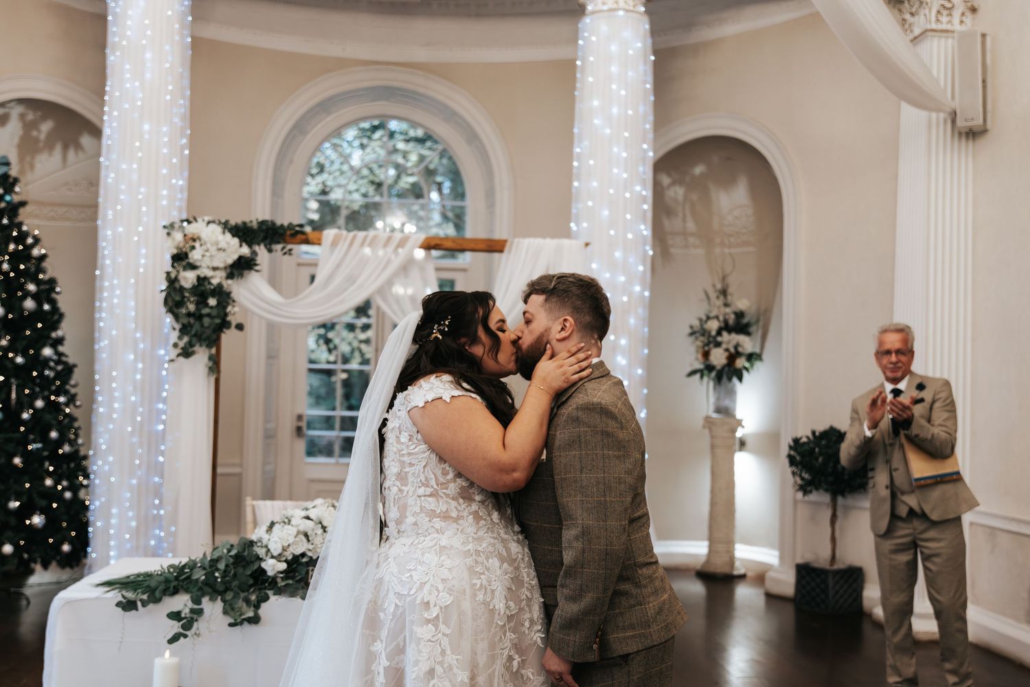 Wedding ceremony in an elegant white room with twinkle lights and floral decorations.