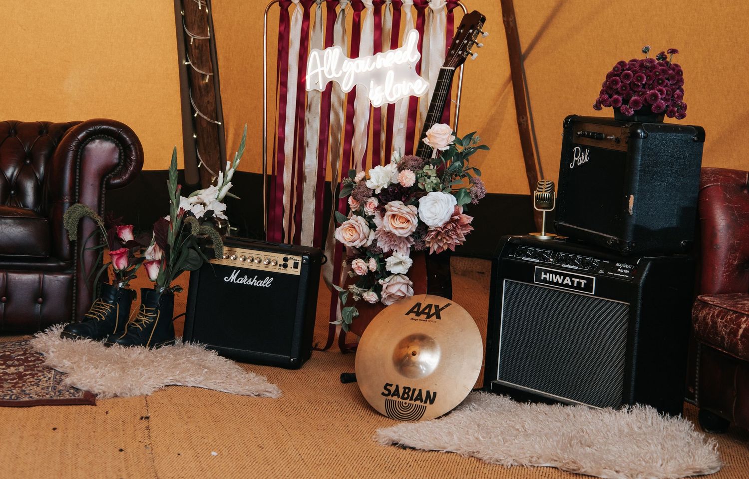 Music setup with Marshall amps, cymbals, and floral arrangements against red and white striped backdrop.