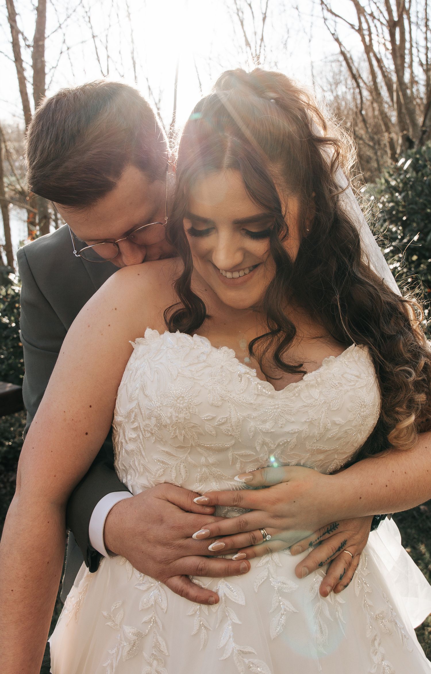 Intimate sunlit moment between newlyweds in formal attire outdoors.