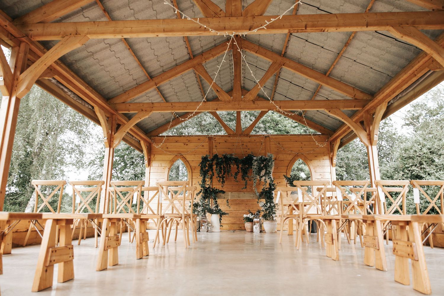 Rustic wooden wedding venue with exposed beam ceiling, cross-back chairs, and floral arch altar.