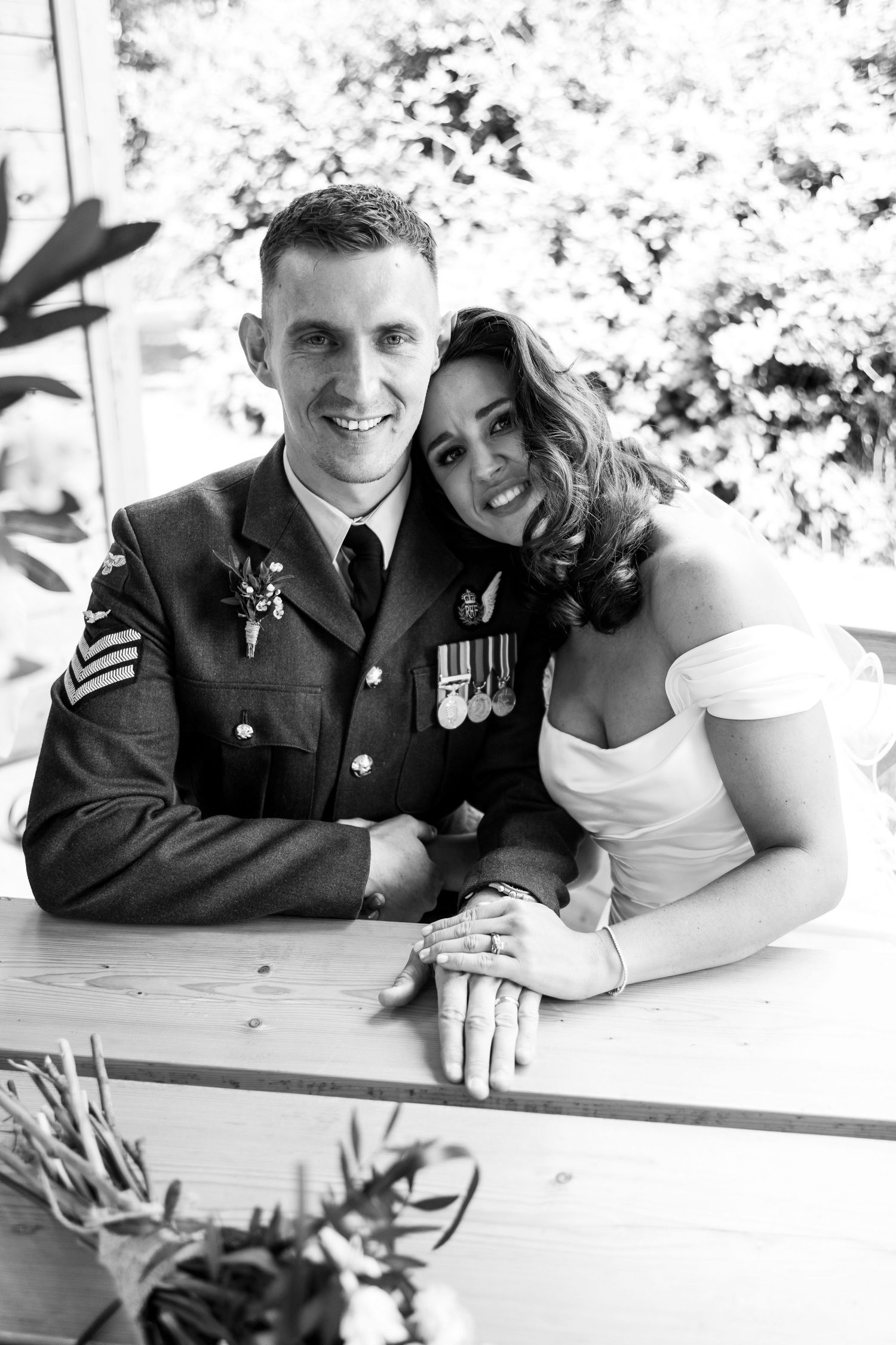 Black and white wedding photo of a smiling military groom in uniform with medals and bride in white dress.