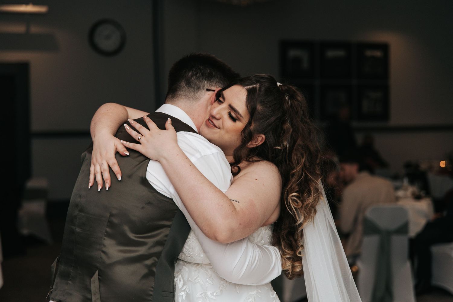 A tender embrace between newlyweds during their first dance at a dimly lit reception venue.