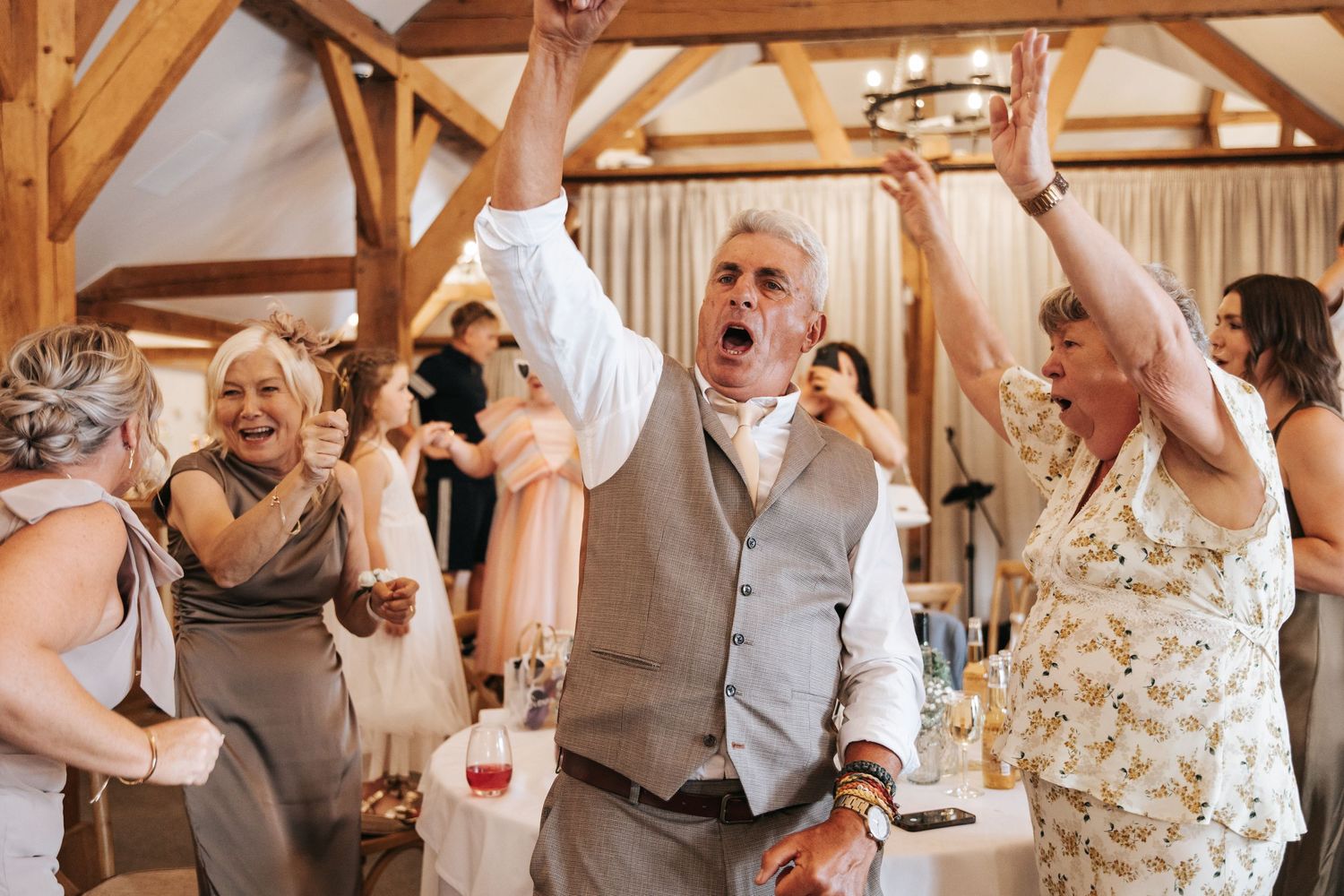 Joyful wedding guests dancing and celebrating with raised arms in a rustic barn venue.