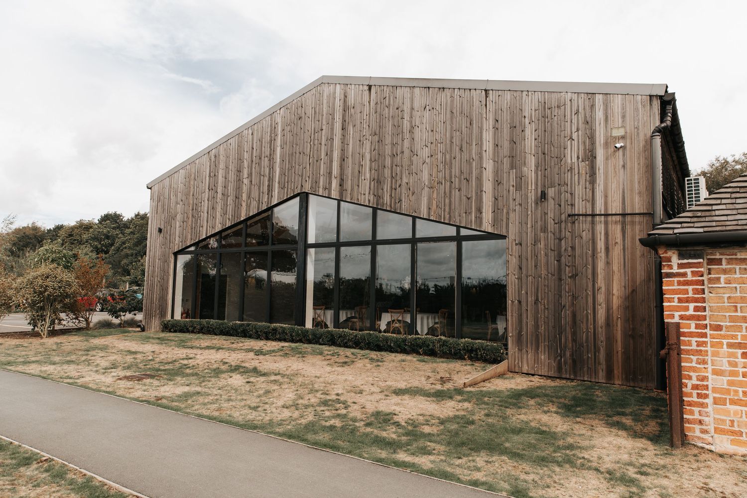 Modern barn-style building with weathered wood cladding and large black-framed glass windows set in a rural landscape.