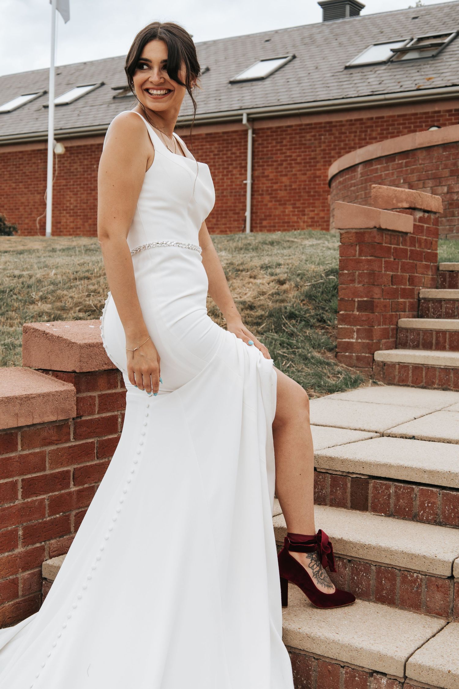 Bride in elegant white dress poses playfully on brick steps outdoors.